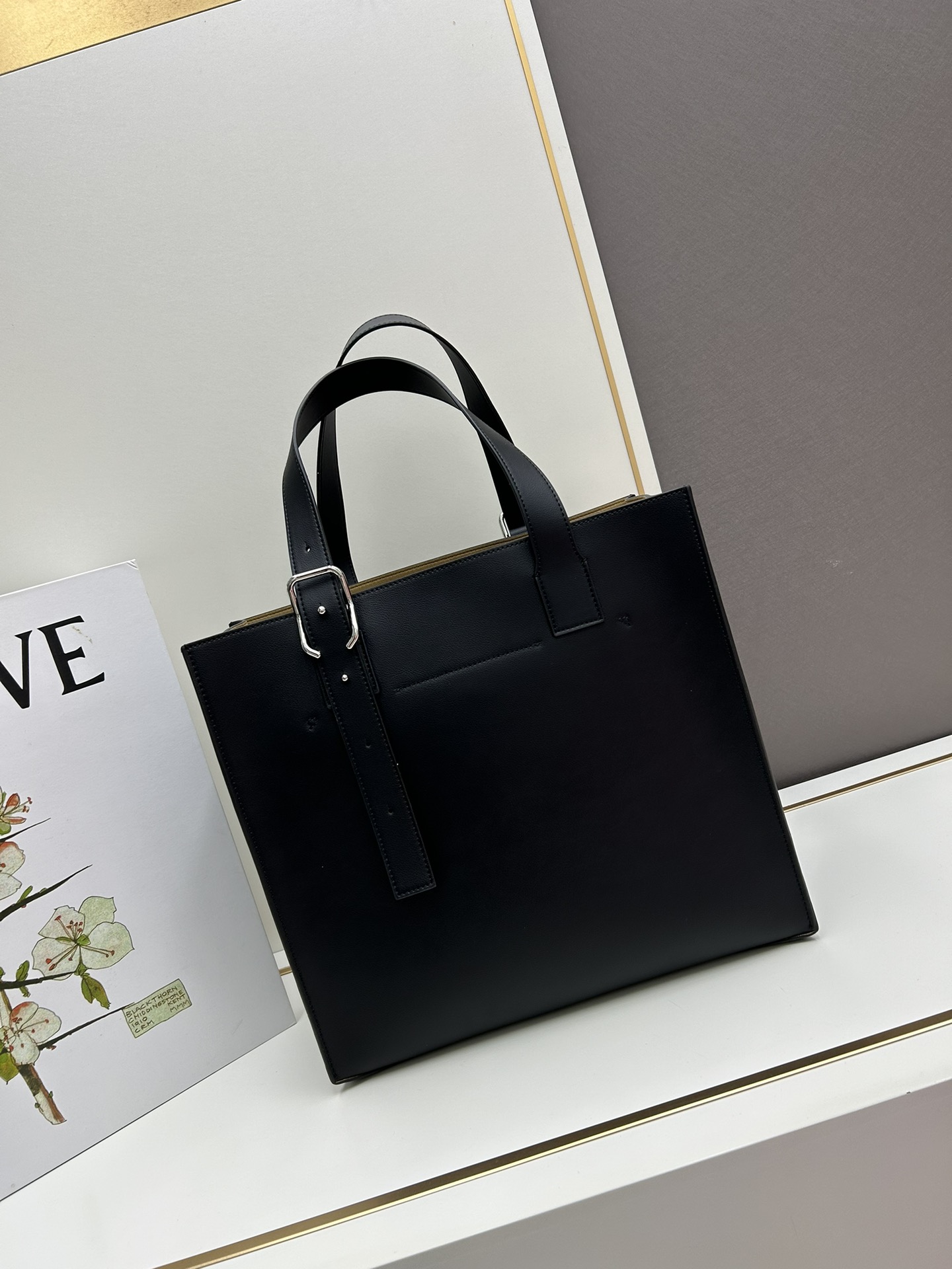 780 Loewe Buckle Tote 不带拉链 荔枝纹深灰手袋 男仕灰色托特包，型號3050 宽大的容量和纤细的轮廓。扁平和不对称的双顶部手柄，饰有标志性的弧形开口搭扣，可通过链扣调节，适合不同的携带方式。主要特点：偏宽扁平矩形包身，内部拉链口袋，两个缝合插袋隔层，真皮里里，Anagram压印点缀 尺寸36-33-17cm