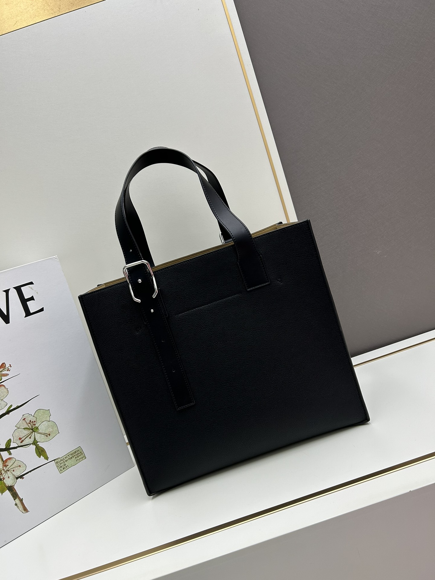 780 Loewe Buckle Tote 不带拉链 荔枝纹深灰手袋 男仕灰色托特包，型號3050 宽大的容量和纤细的轮廓。扁平和不对称的双顶部手柄，饰有标志性的弧形开口搭扣，可通过链扣调节，适合不同的携带方式。主要特点：偏宽扁平矩形包身，内部拉链口袋，两个缝合插袋隔层，真皮里里，Anagram压印点缀 尺寸36-33-17cm