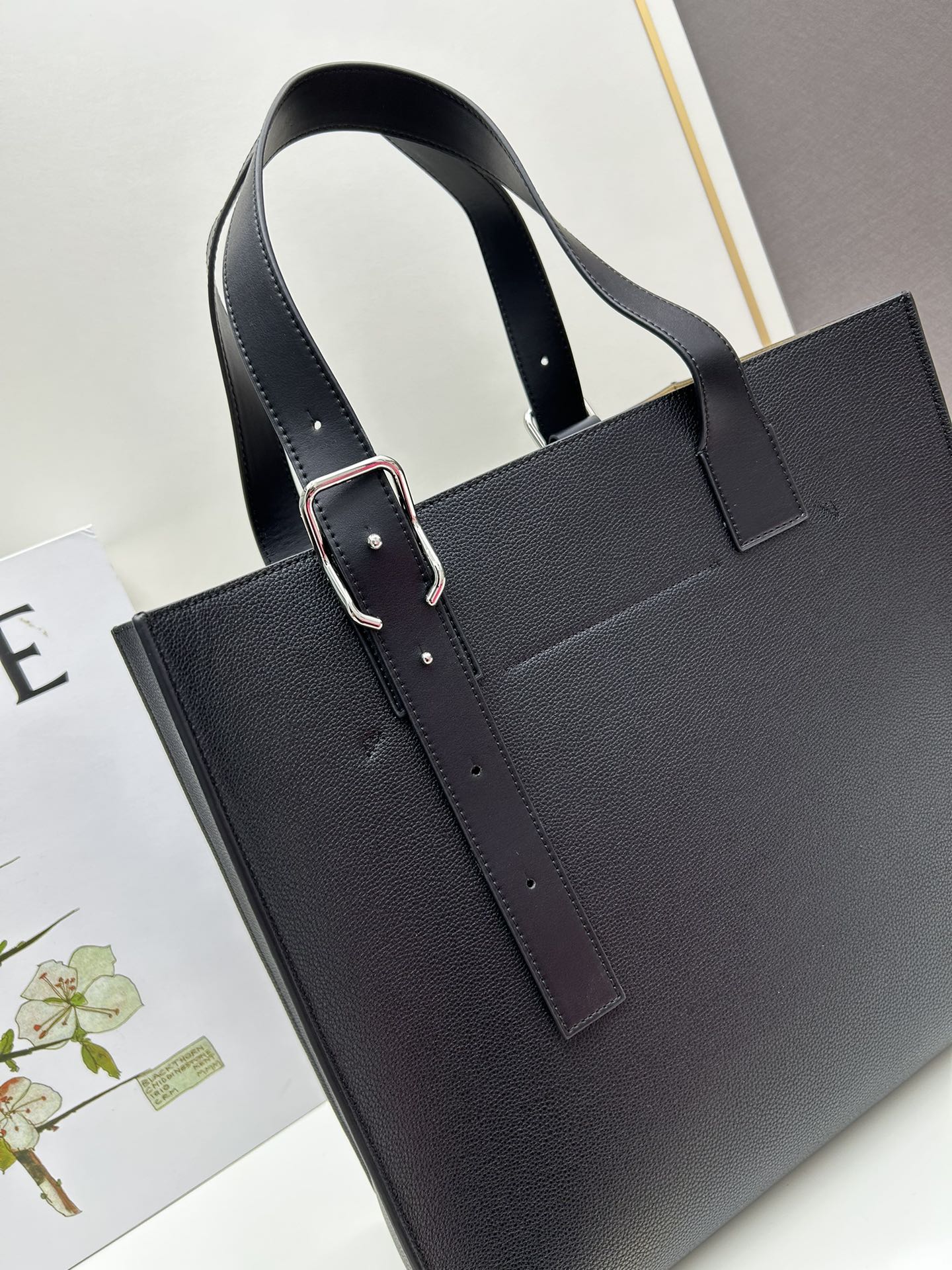 780 Loewe Buckle Tote 不带拉链 荔枝纹深灰手袋 男仕灰色托特包，型號3050 宽大的容量和纤细的轮廓。扁平和不对称的双顶部手柄，饰有标志性的弧形开口搭扣，可通过链扣调节，适合不同的携带方式。主要特点：偏宽扁平矩形包身，内部拉链口袋，两个缝合插袋隔层，真皮里里，Anagram压印点缀 尺寸36-33-17cm