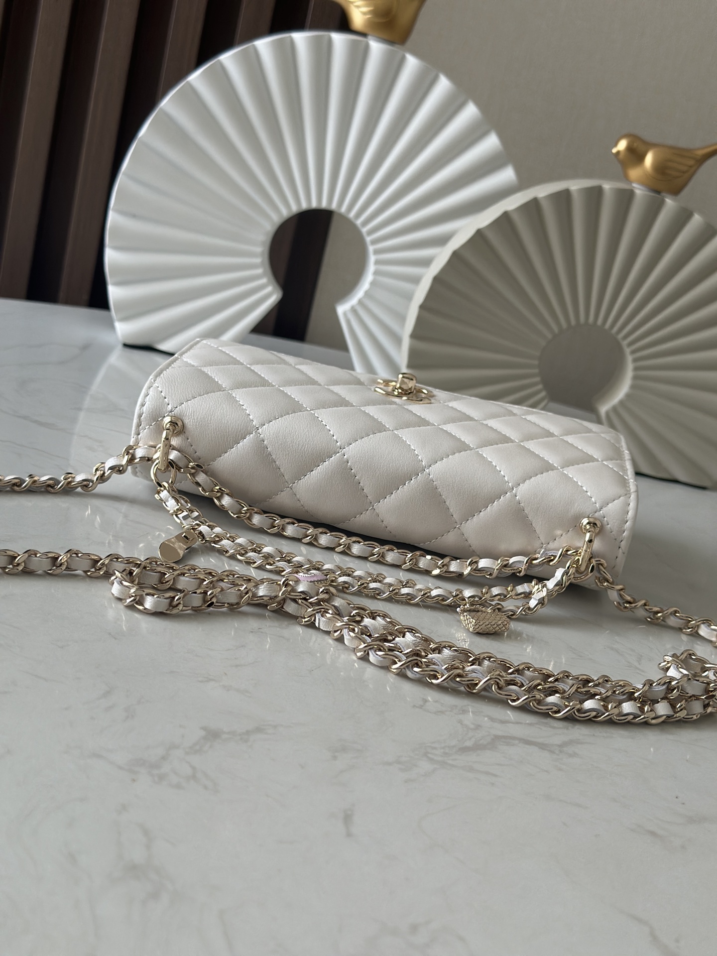p670。chane12025春夏
chanel 太懂少女心!2025年春夏的轻巧俏
皮又精致，采用珠面小羊皮，搭配经典的菱格纹和金色 clogo。手袋上还有一个粉色心形，搭配金色链条，让人一见倾心，入坑!还可
以侧背或肩背，容量也不错，纸巾都可以放进去，通勤日常都ok
款号：66051 白色
尺寸:19.5*13*3.5

