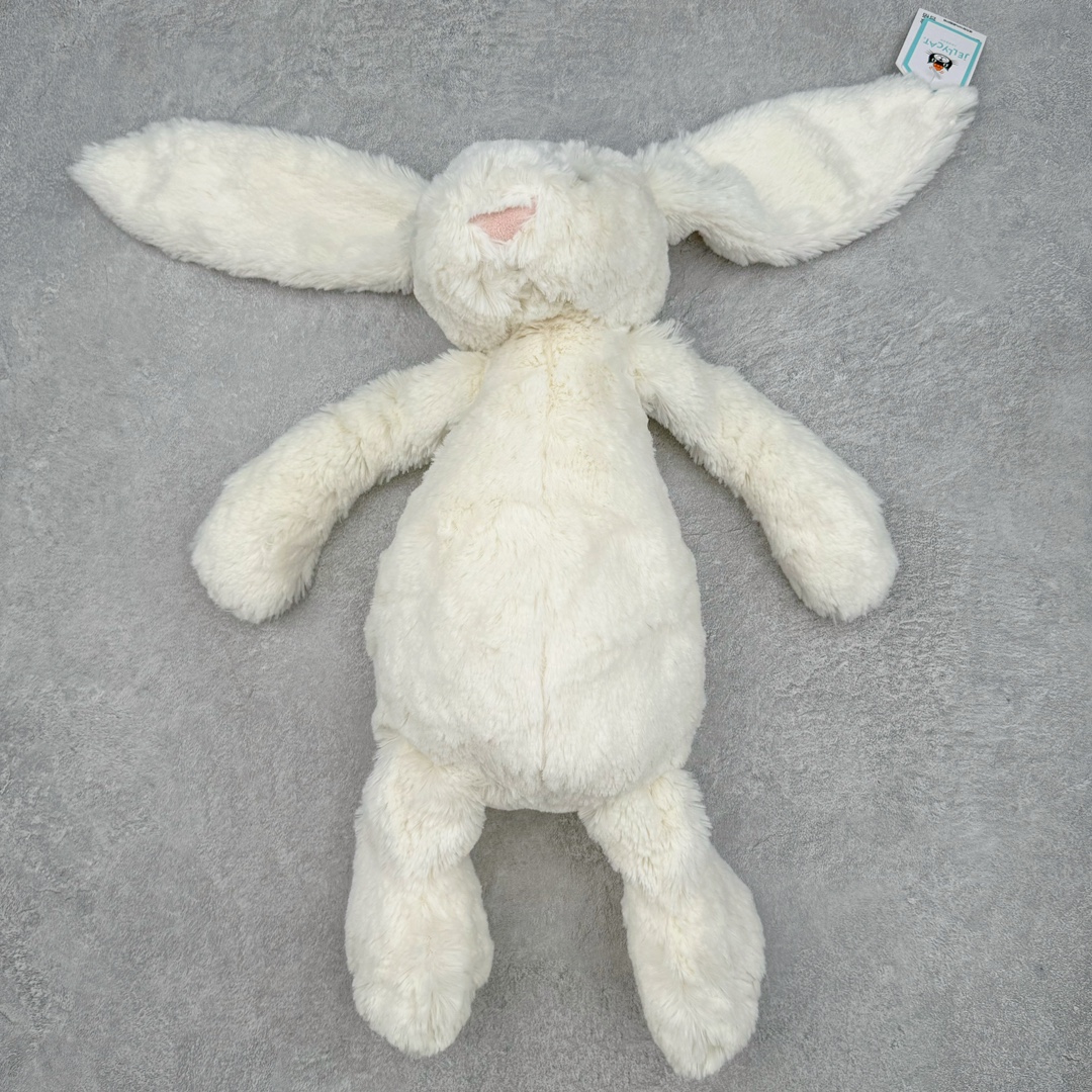 ＃原单 Jellycat 玩偶 毛绒公仔 邦尼兔 31CM 科普：Jellycat是一个英国玩具品牌，创立于1999年，由William和Thomas兄弟二人在伦敦创立。该品牌专注于设计玩偶玩具，并全情投入于最有趣、环保和独特的软玩具领域。Jellycat的产品设计丰富且有创意，其毛绒玩具以可爱的动物形象为主打，深受全球儿童的喜爱。品牌的产品线包括各种动物系列、海洋系列、蔬果美食系列、植物系列等，每个系列都有其独特的设计和故事。Jellycat的产品设计理念是打破传统动物毛绒像动物标本一样的形象，通过改变形状、手感、颜色、大小和材料，用成千上万种方式制作一只动物毛绒。品牌的设计师来自世界各地，他们的创意让产品更具多元性，同时也让品牌能够从世界各地的文化中获得设计灵感。近年来，Jellycat品牌方开始跨界合作，与野兽派、华尔道夫酒店等品牌合作推出联名产品，进一步扩大了品牌的影响力。在社交媒体上，Jellycat也日益活跃，通过小红书、Instagram、抖音和TikTok等平台与消费者互动，分享品牌故事和产品信息。Jellycat的产品价格在99元到1699元不等，绝版产品的价格在二手平台上甚至会翻几倍。尽管有消费者认为它高价低质，价格贵、品控不严格等问题频频引来吐槽，但仍有大量粉丝愿意为“治愈”买单，因为这些毛绒玩具成为他们精神上的陪伴。原装100% polyester进口聚酯纤维面料 原厂7D棉 原单环保颗粒 双吊牌加三重水洗标 原配防尘袋 吊打市面通货 注意即使同一家厂 不同的批次面料缸差是一定都有的 官网不同批次都有 经过欧盟CE安全认证 此标准0-100岁的小朋友都适用 这个缸差和造型其实经常入手玩偶的都知道 手工制品 世上每一只jell 都是独一无二的 轻微线头 轻微不对称都是很正常的 无法避免 官网都是一样 底部走线 颗粒填充物 刺绣 走线 肉眼可见的精致 原色未染色面料纱线 超级有质感-选品中心