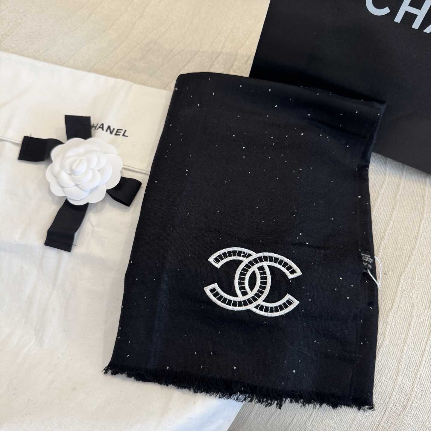 这是Chanel经典款黑色双C闪片围巾，黑底上分布着细腻闪片星光，中间是标志性双C交织Logo，边缘带流苏设计，低调中带