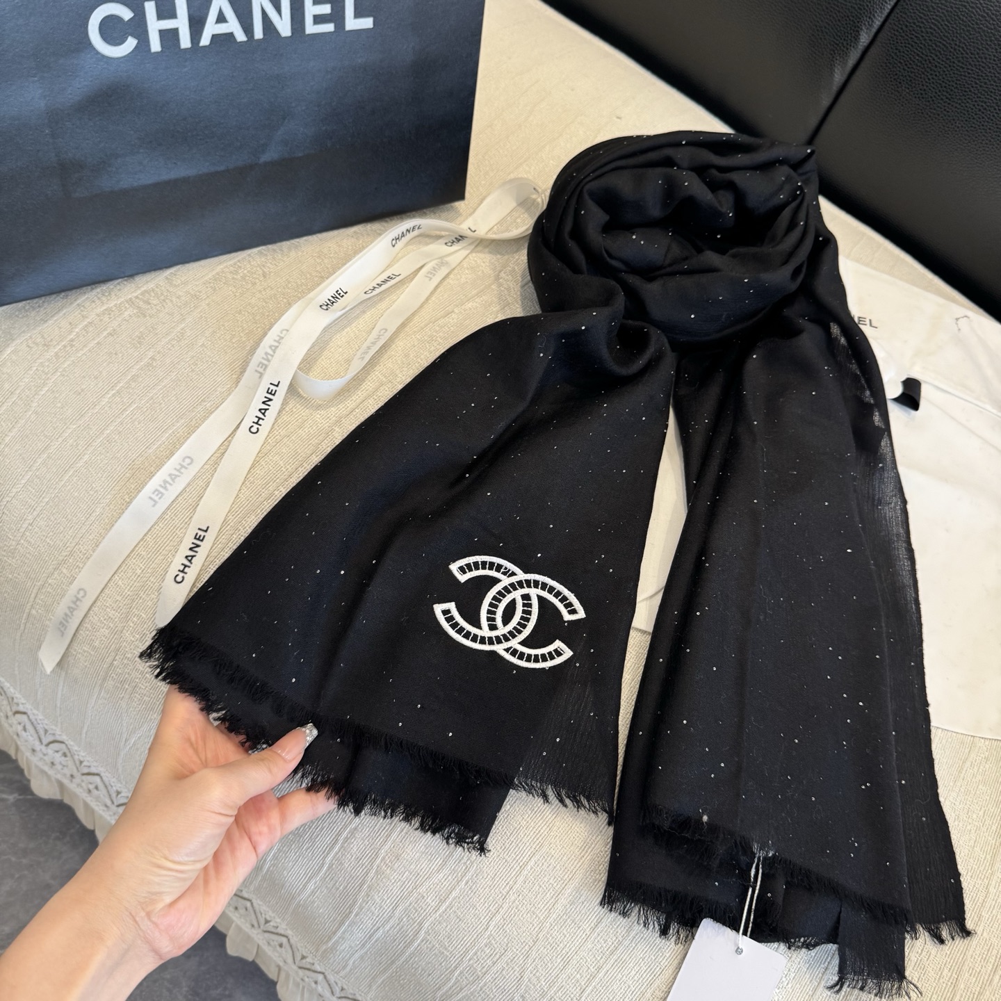 这是Chanel经典款黑色双C闪片围巾，黑底上分布着细腻闪片星光，中间是标志性双C交织Logo，边缘带流苏设计，低调中带