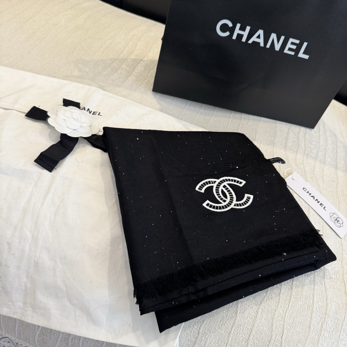 这是Chanel经典款黑色双C闪片围巾，黑底上分布着细腻闪片星光，中间是标志性双C交织Logo，边缘带流苏设计，低调中带