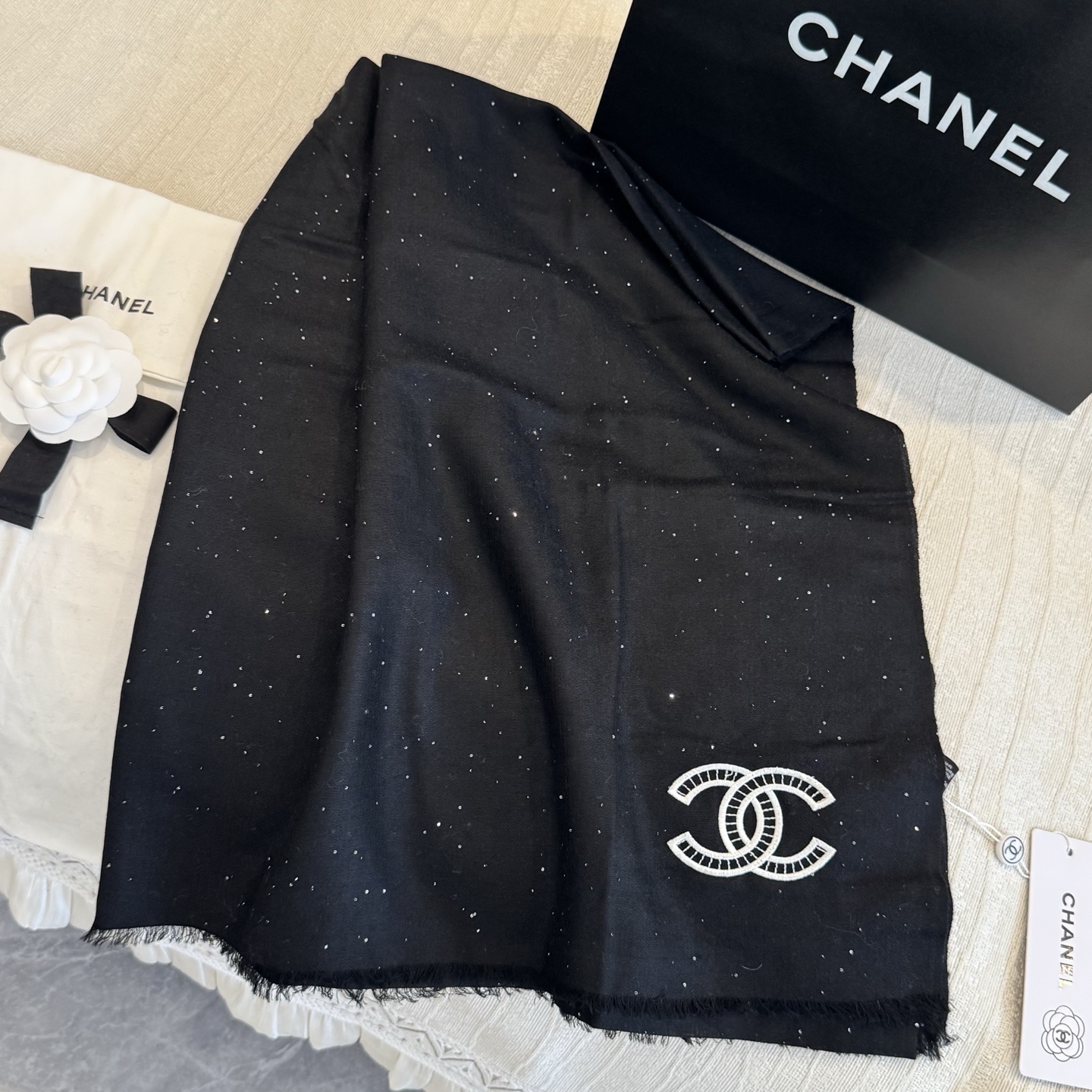 这是Chanel经典款黑色双C闪片围巾，黑底上分布着细腻闪片星光，中间是标志性双C交织Logo，边缘带流苏设计，低调中带