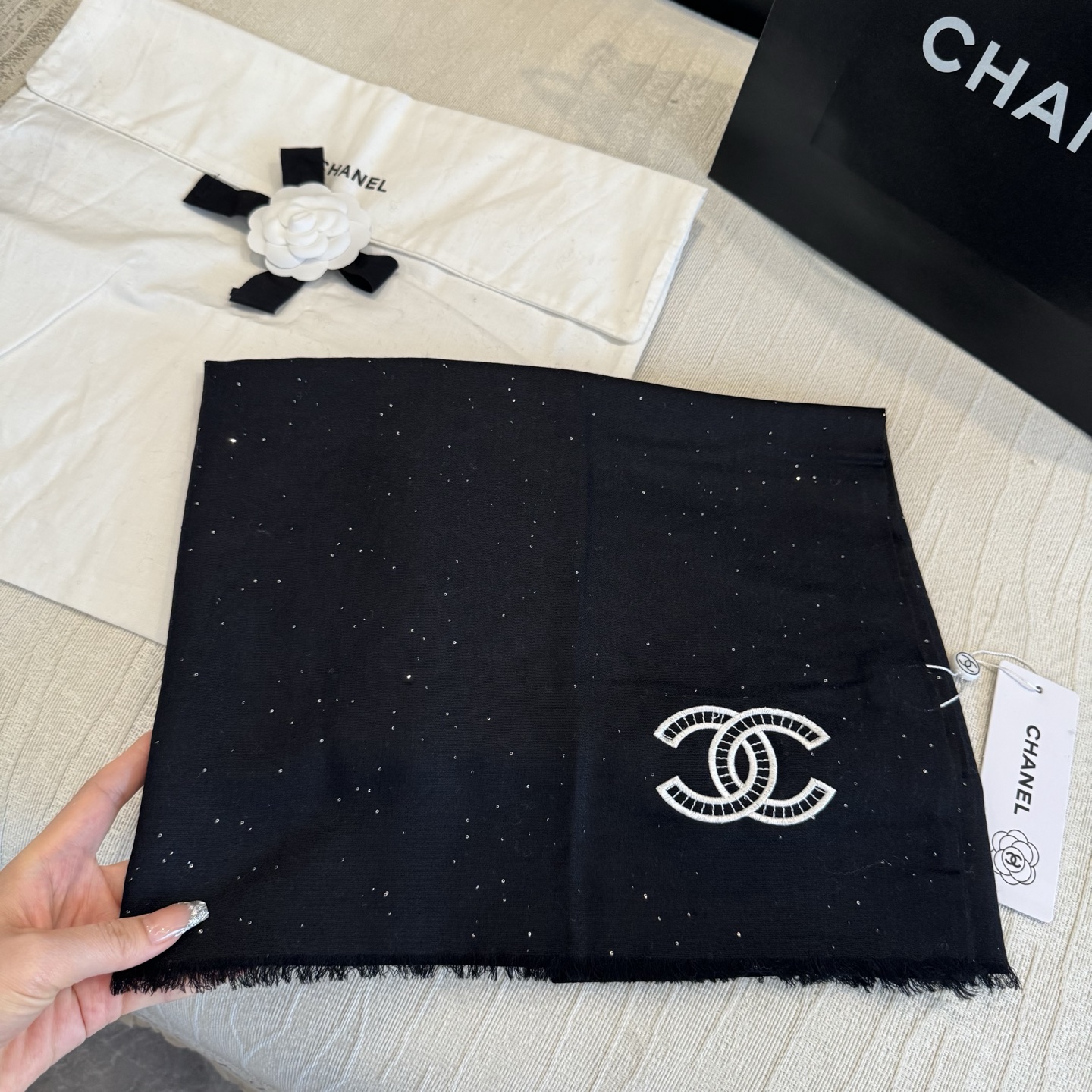 这是Chanel经典款黑色双C闪片围巾，黑底上分布着细腻闪片星光，中间是标志性双C交织Logo，边缘带流苏设计，低调中带