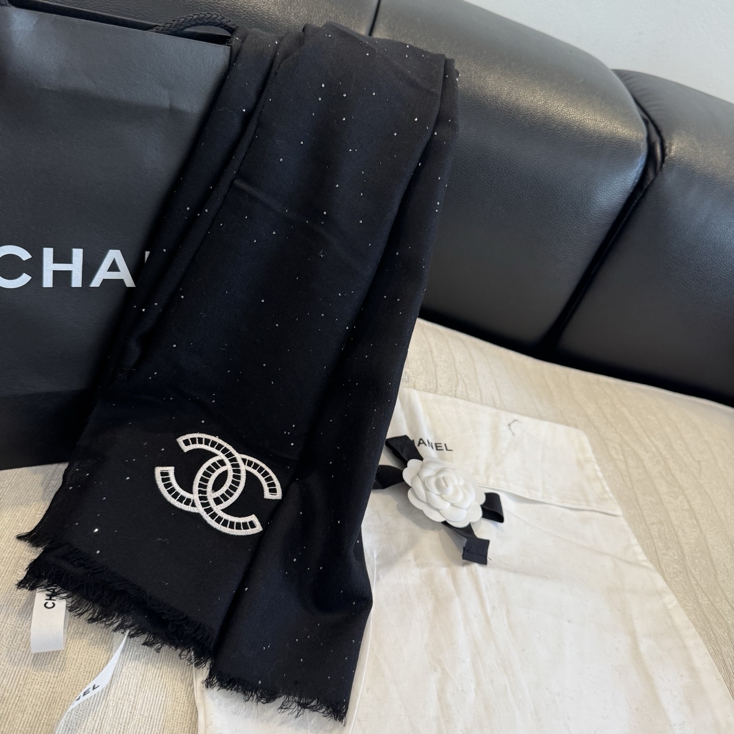 这是Chanel经典款黑色双C闪片围巾，黑底上分布着细腻闪片星光，中间是标志性双C交织Logo，边缘带流苏设计，低调中带