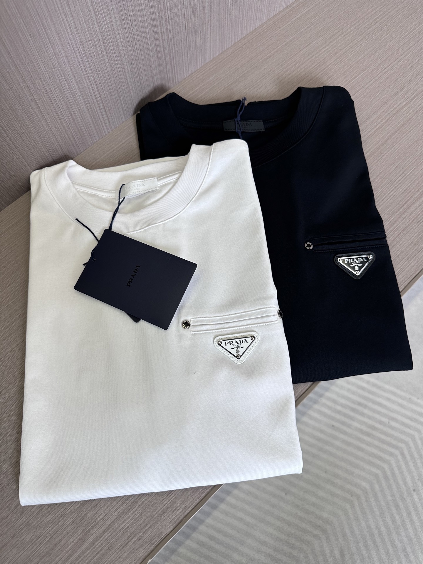 NO:441779,PRA25SS spring and summer new jersey cotton basic round neck short Tee, men and women's same triangle fake pocket casual pullover short-sleeved T-shirt!  P Home's new T-shirt has won wide praise for its exquisite fabrics, clever design and comfortable fit!  It is not only a single item worth having in daily matching, but also an indispensable choice to show personal taste and style!  This short Tee is made of fixed-woven and dyed jersey cotton, with a solid and soft feel, and has an overall breathable and hygroscopicity!  In terms of auxiliary materials, the same color dyed ribbed round collar splicing design is designed for long-lasting washing and not easy to deform!  The fake pockets on the chest are combined with the brand triangle badge and embellished on the clothes, eye-catching and eye-catching, and are the finishing touch!  This T-shirt is made of a basic straight-fitting tailoring, which can be easily controlled by both men and women. Whether paired with casual pants or trousers, it can show a sense of fashion and taste!  Not only that, but also highlights the elegant and relaxed atmosphere under the comfortable wearing experience!  Black/white, two colors into it!  Size S-XXL S S shoulder width 45cm-bust 102cm-length 68cm M S shoulder width 46cm-bust 106cm-length 70cm L S shoulder width 47cm-bust 110cm-length 72cm XL S shoulder width 48cm-bust 114cm-length 74cm XXL S shoulder width 50cm-bust 118cm-length 76cm Size recommended (standard version) Height 174-140 catties, try on M size appropriately!  A boy can choose S code within 130 catties, a M code for 130-143 catties, a L code for 143-156 catties, a XL code for 156-170 catties, and a XXL code for 170-185 catties!  All girls can choose S code!  ,,prada,T-shirt,tees,t-shirt,alexander wang19860909PRA25SS春夏新款平纹针织棉布基础圆领短Tee,男女同款三角标假口袋休闲套头短袖T恤衫！P家新款T恤以其精湛的面料、巧妙的设计和舒适的版型赢得了广泛好评！它不仅是日常搭配中值得拥有的单品,更是展现个人品味和风格的不可或缺之选！ 该短Tee采用定织定染平纹针织棉布制成,手感瓷实柔软,整体透气吸湿性佳！辅料方面,同缸色染罗纹圆领拼接设计,经久耐洗不易变形！胸前的假口袋与品牌三角标徽章相结合,点缀在衣服上,醒目吸睛,堪称点睛之笔的存在！这款T恤采用基础直筒版型剪裁,男女都能轻松驾驭,无论是搭配休闲裤还是西裤,都能展现出时尚感和品味！不仅如此,在舒适的穿着体验下也凸显出优雅与轻松的氛围！黑色/白色,两色入！尺码S-XXL  S码肩宽45cm-胸围102cm-衣长68cm M码肩宽46cm-胸围106cm-衣长70cm L码肩宽47cm-胸围110cm-衣长72cm XL码肩宽48cm-胸围114cm-衣长74cm XXL码肩宽50cm-胸围118cm-衣长76cm 尺码推荐（标准版型） 身高174-140斤,试穿M码合适！ 男生体重130斤以内选择S码,130-143斤选择M码,143-156斤选择L码,156-170斤选择XL码,170-185斤选择XXL码！ 女生全部选择S码即可！,,prada,T-shirt,tees，t-shirt,alexander wang,Men's clothing