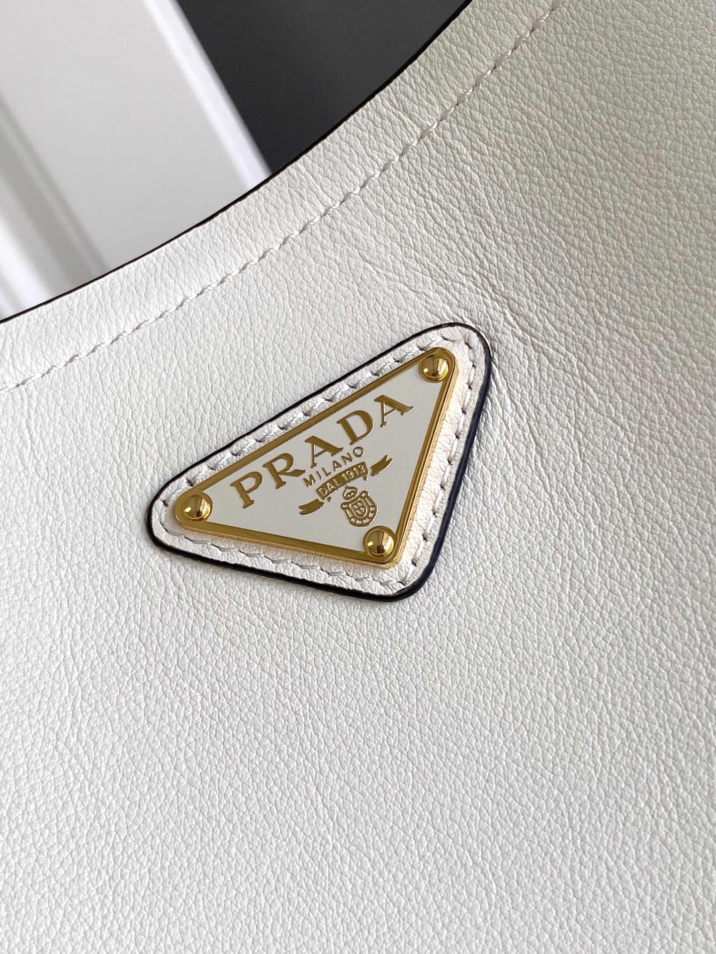 Prada 这款皮革手袋拥有柔和线条与精美设计，凸显 格调与手工细节。实用百搭，饰有涂珐琅三角形金属徽标，增添辨识度