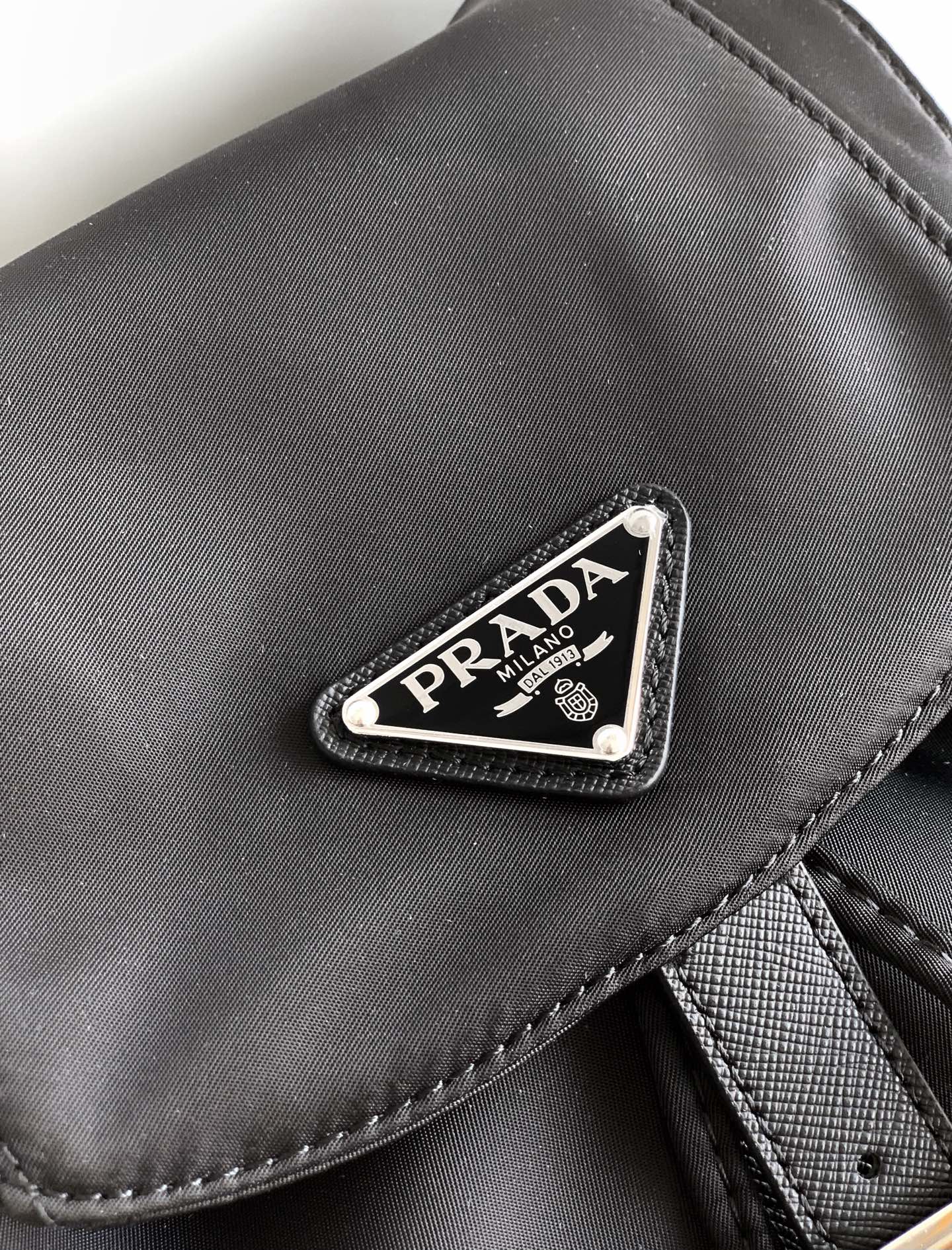 Prada 这款尼龙双肩包采用 Saffiano皮革饰边 融合多种材质 并饰有三角形徽标