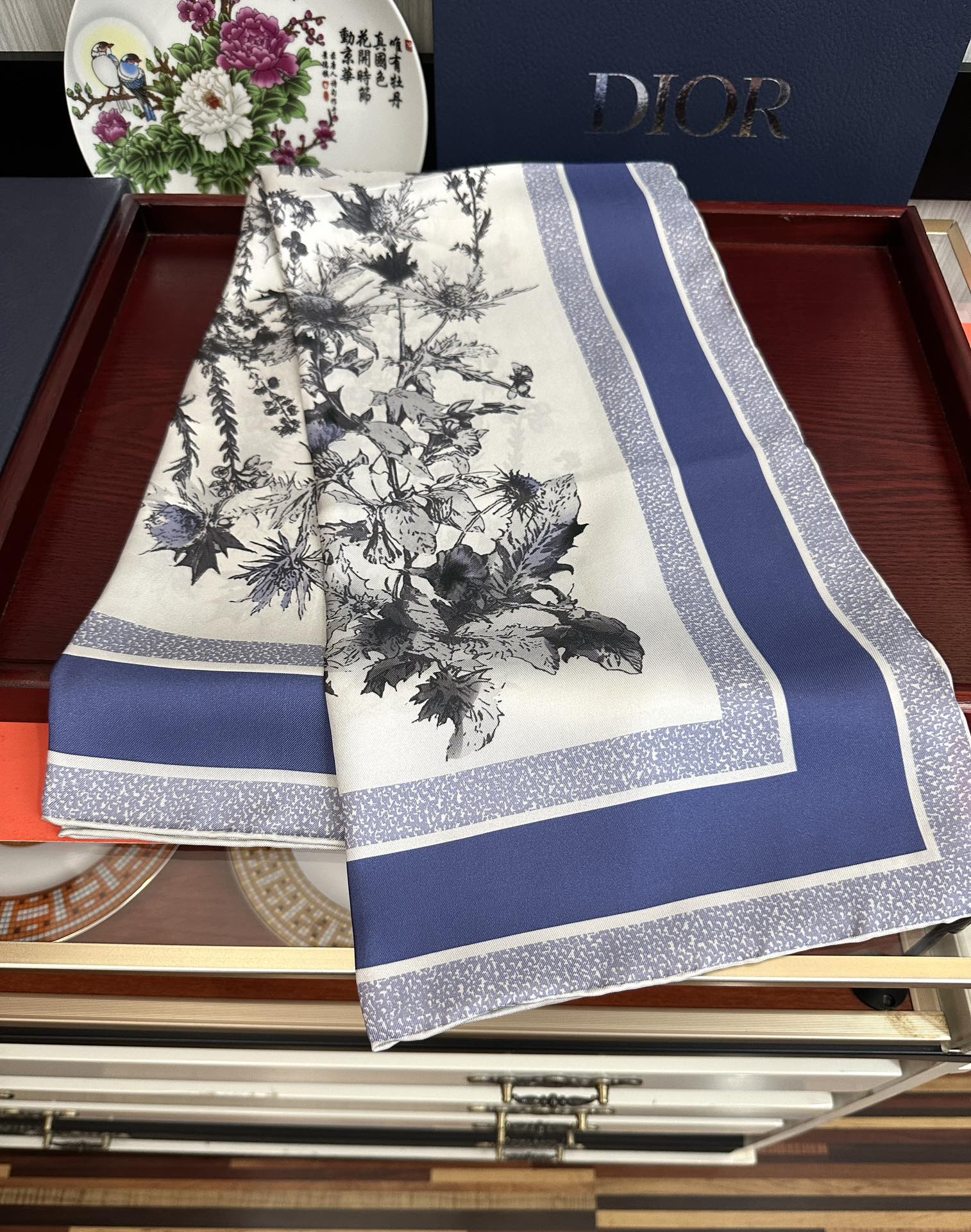 Dior 高版本Dior Chardons 图案印花 展示象征着保护、韧性和自由的苏格兰国花 采用白色和蓝色桑蚕丝斜纹面料精心制作 双面设计搭配手工卷边 点缀以对比鲜明的 Christian 标志提花条形图案提升格调 可系在颈部或作为头巾使用 打造 的 造型
