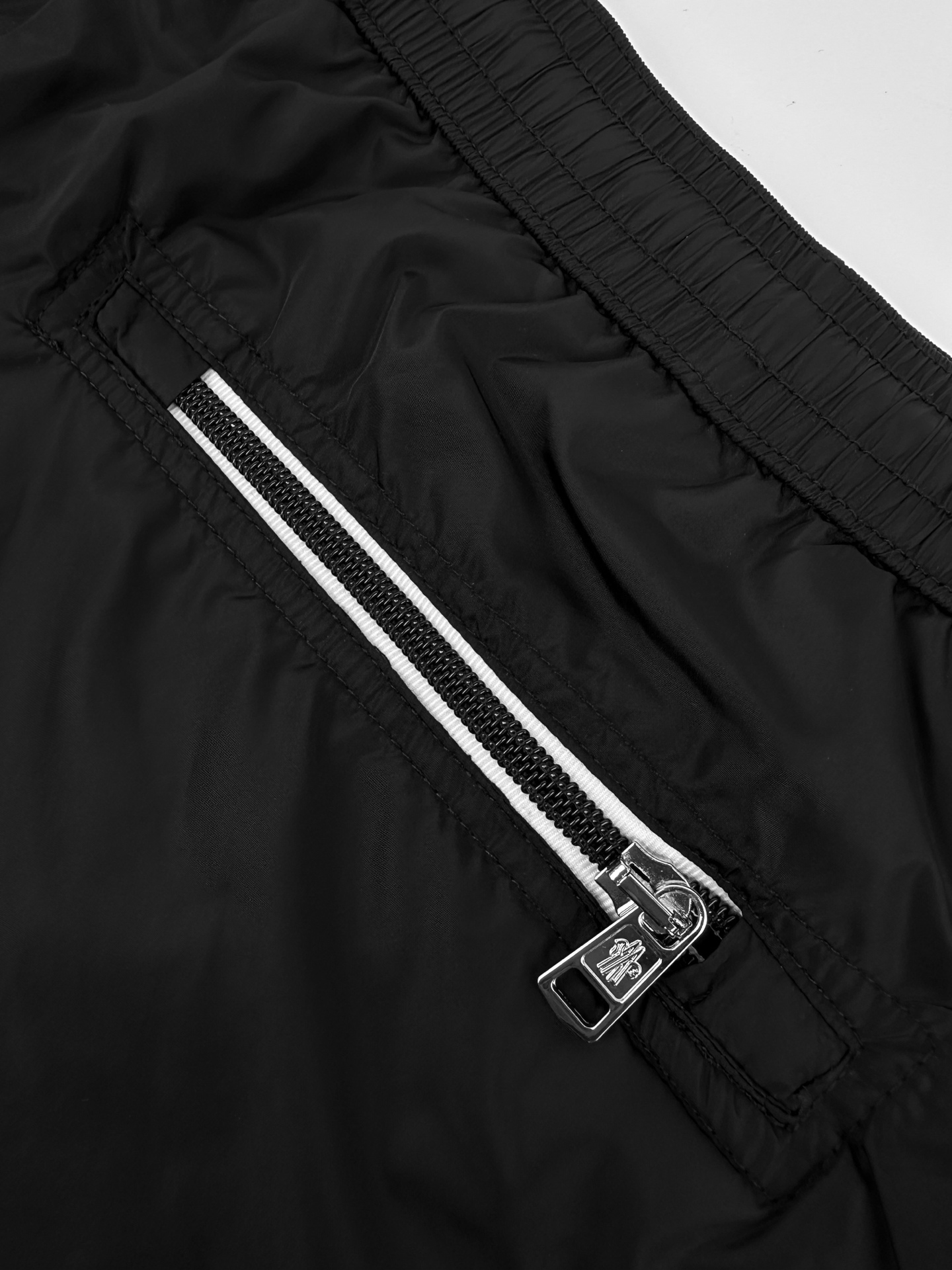 Moncler 定制冰壤棱织尼龙 搭配细密网布衬里 清爽透气 舒适贴肤 以深邃的黑为主色调 纯粹而深邃 标志性Moncler标识贴片轻缀裤身 瞬间为整体造型注入灵魂 彰显品牌魅力 背面巧妙融入拉链口袋 辅以三色饰边点缀 增添层次与动感 每一处细节都是对传统工装的反叛 以轻盈之姿解锁夏日百变奢雅