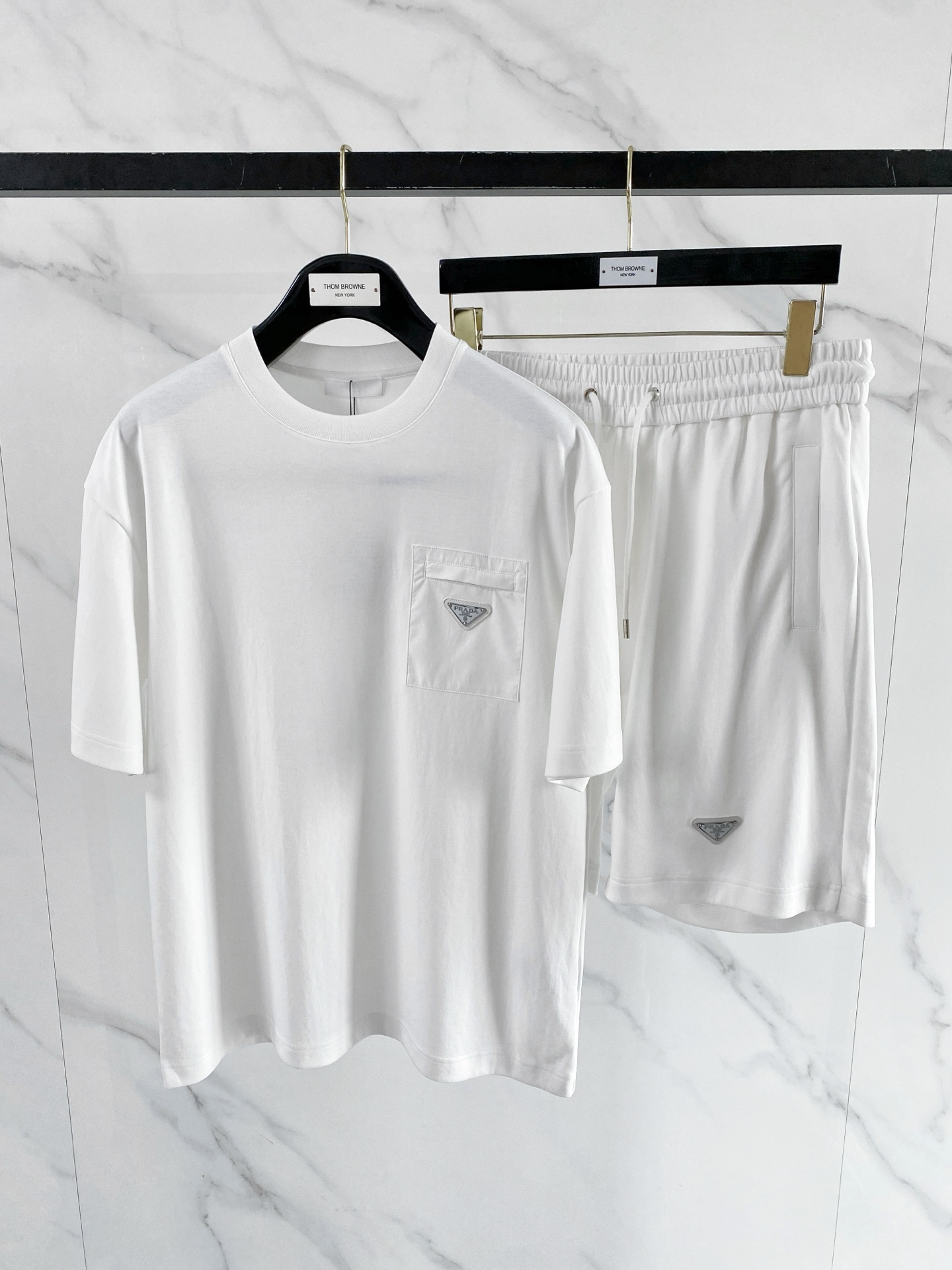 NO:848808,/ Set Prada 1956 Spring and Summer | Prada Triangle Pocket Set A set that captures the 'effortless sense of luxury'. The T-shirt is made of soft, skin-friendly high-count cotton, paired with tencel-like draped shorts of the same color. The nylon stitching on the pocket + the iconic triangle logo are low-key and recognizable. Available in black and white, the white is refreshing and clean, and the black is neat and cool. The whole set is effortless to wear out, relaxed and elegant.  Size 48-56,,prada,prada,shorts,tees,t-shirt,19860909/套 Prada 普拉达1956 春夏｜Prada 三角标口袋套装 一套把“不费力的高级感”拿捏了. T恤是软糯亲肤的高支棉,搭配同色系天丝感垂坠短裤,口袋处的尼龙拼接+标志性三角标,低调又有辨识度. 黑白两色,白的清爽干净,黑的利落酷感,整套穿出门不用费脑搭配,松弛又显贵. 码数48-56,,prada,prada,shorts,tees，t-shirt,,Men's clothing