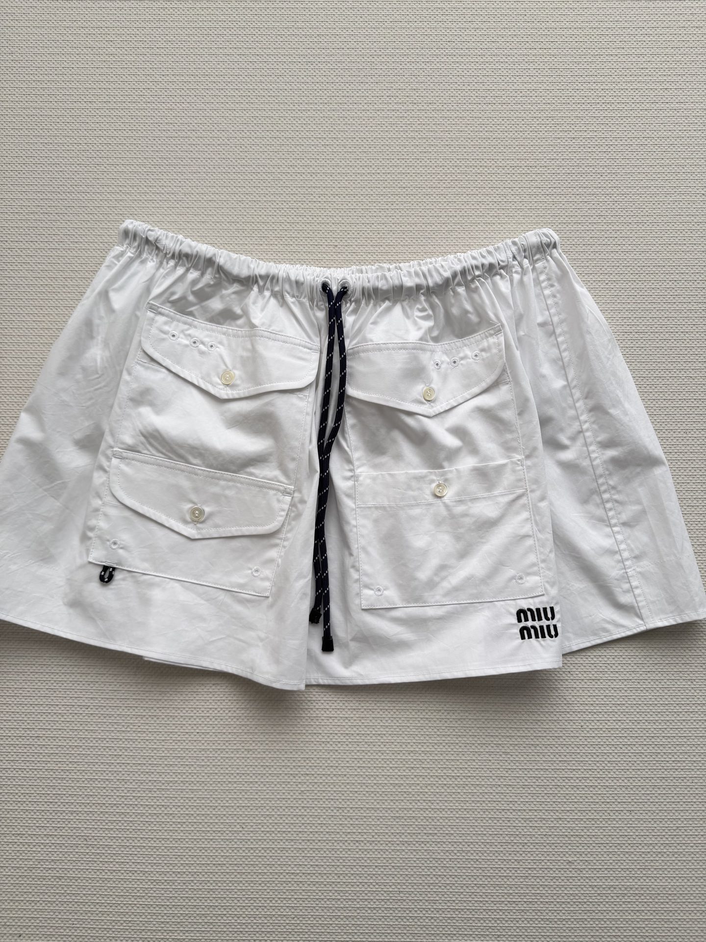 Miu Mi*🆕这款白色工装半裙，采用轻薄科技府绸，触感柔软又挺括。A字版型+松紧腰，舒适显瘦，适合多种