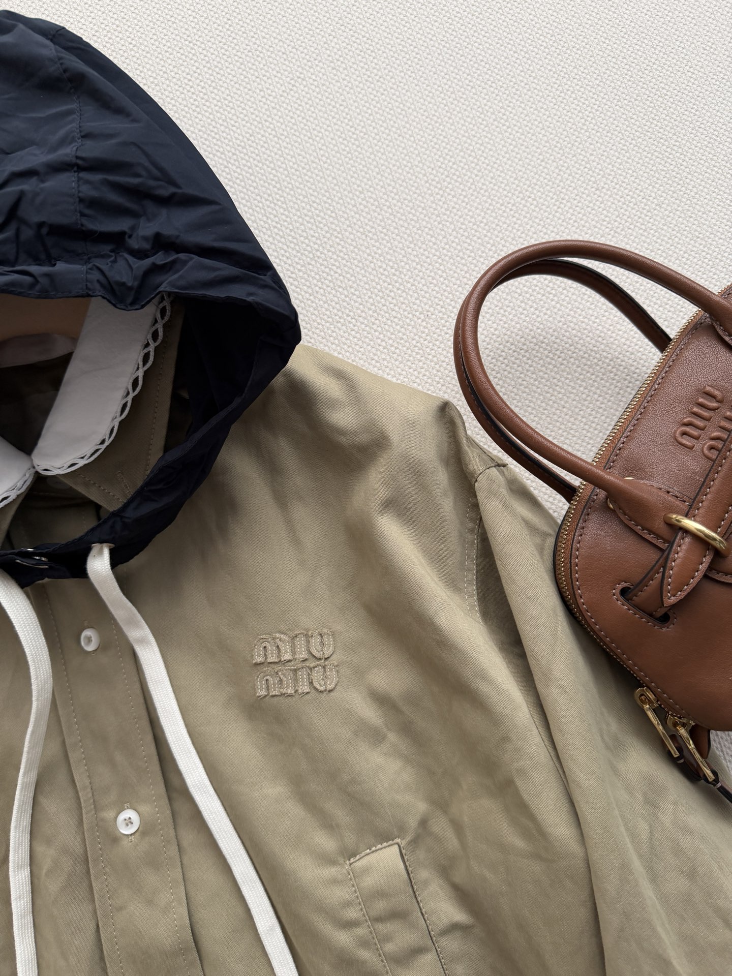 Miu Mi*🆕的卡其色短款工装夹克​​，白色彼得潘领（娃娃领）拼接设计，胸前有 Miu刺绣logo，纽扣开合，下摆松紧