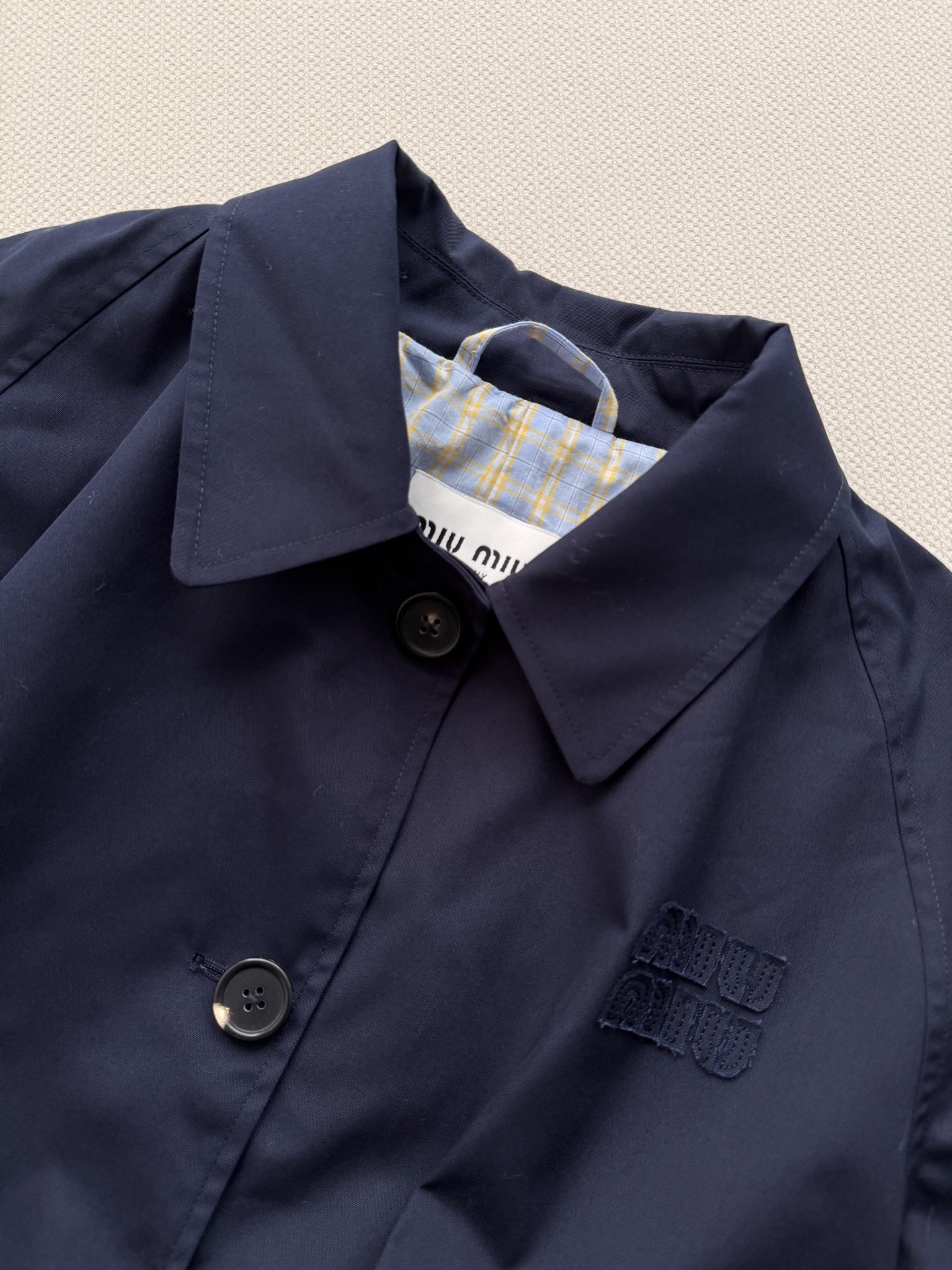 Miu Mi*🆕的藏蓝色长款风衣​​，蓝白格纹拼接翻边设计，属于 Miu比较经典的"假两件"风格风衣。藏蓝色外面是简约的