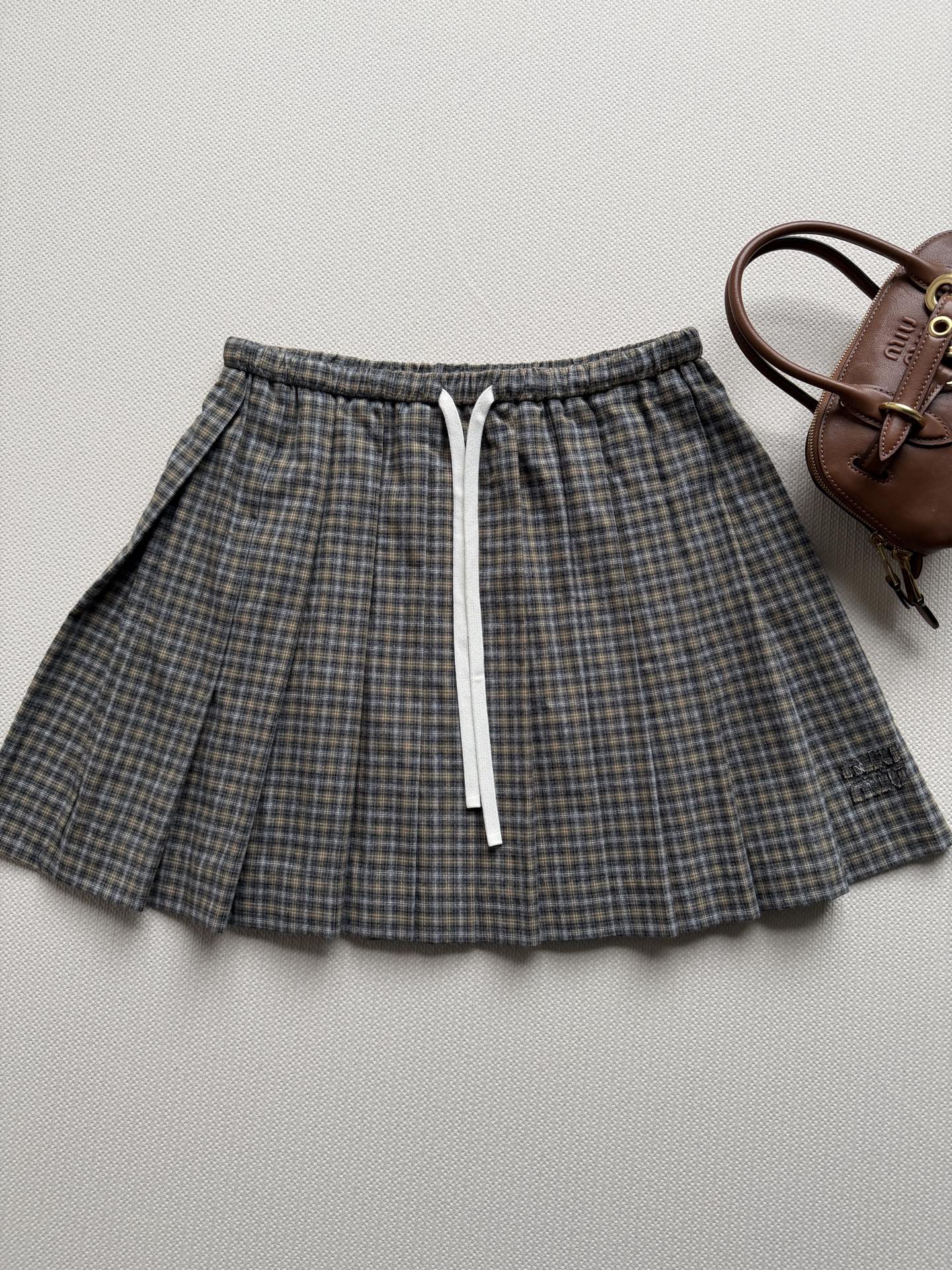 miumi*🆕褶饰细节勾勒这款格纹法兰绒迷你半身裙，灵感源自女装风格准则。撞色运动细节为整体设计画龙点睛，呈现当代学院风