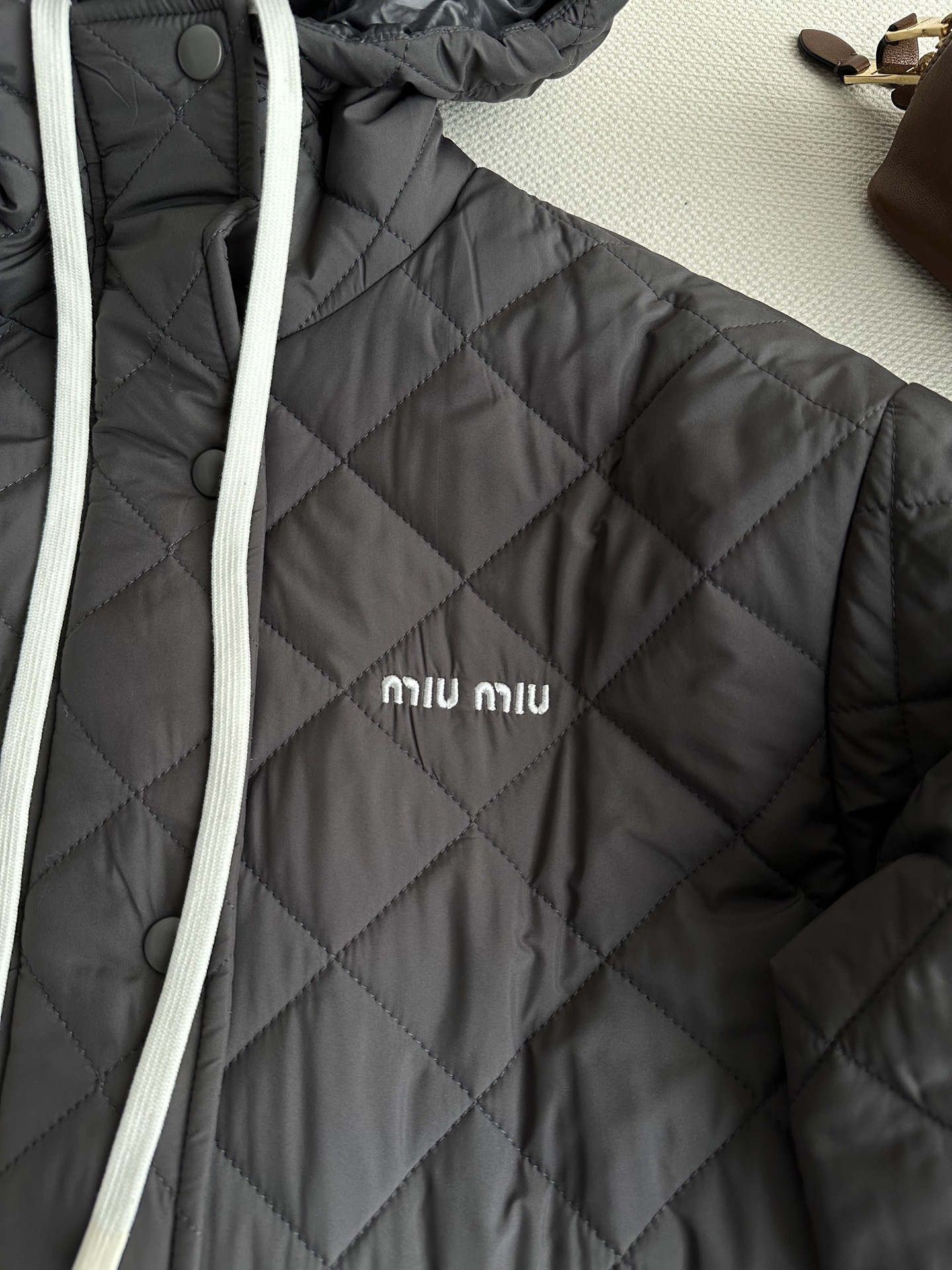 miumi*🆕全身有菱格绗缝压线纹理。连帽设计，白色粗抽绳是整件衣服最跳的视觉亮点。前襟有按扣和拉链两种开合方式。两侧有