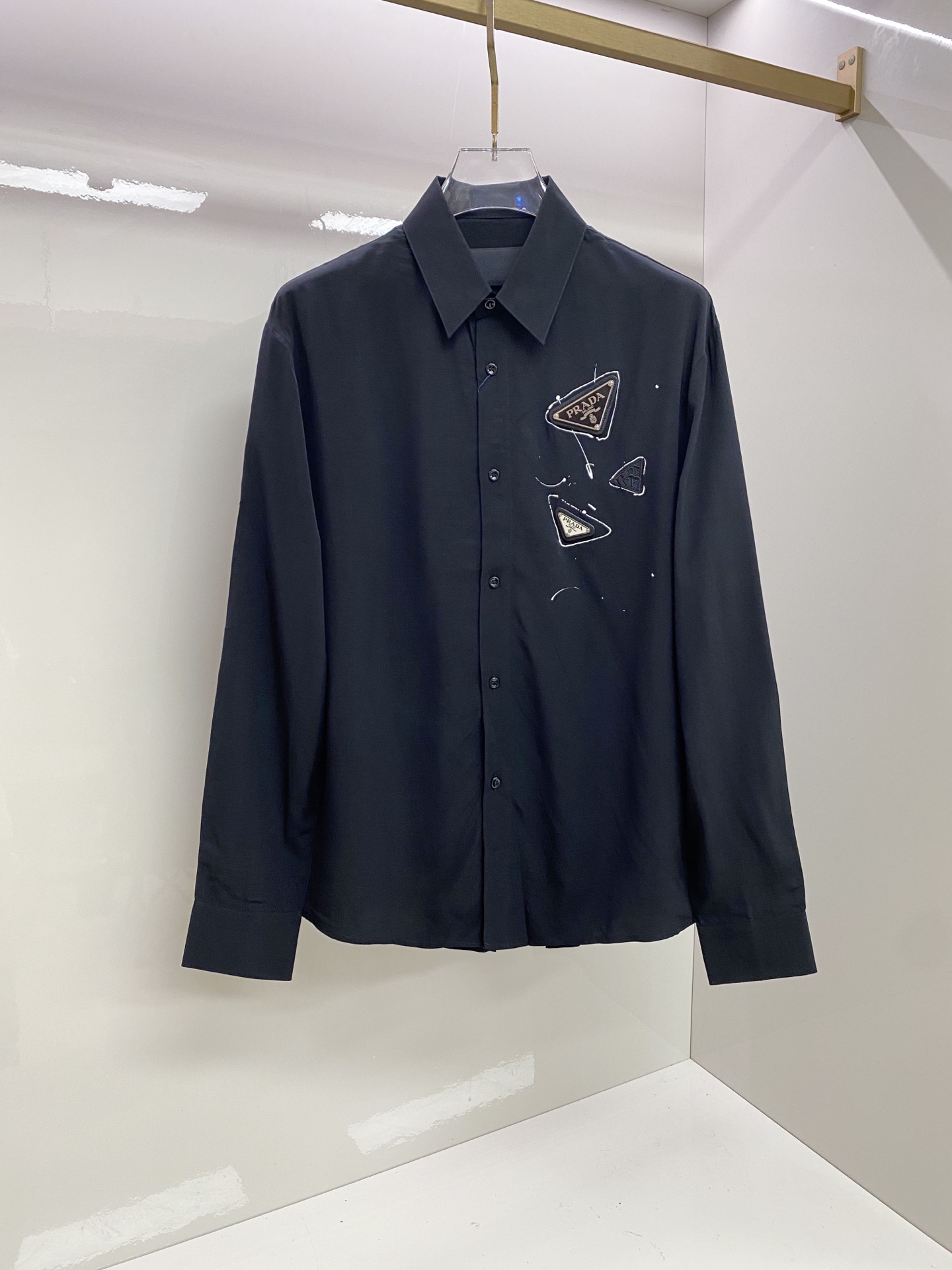 NO:835125,Prada Prada  2026ss spring and summer graffiti triangle logo black shirt, using street graffiti elements and minimalist tailoring to interpret the dark high-end relaxed aesthetics. Made of high-draping matte satin fabric, it feels silky and skin-friendly, has a low-key soft light texture, and the upper body is draped with  shape; the body adopts a neat straight silhouette, and the graffiti-style triangle logo on the chest breaks the dullness and injects street vitality. Whether worn alone to create a cool commuting style, or layered with a suit to create a business elite feel, it can easily create an effortless high-quality outfit.  Size 48-56,,prada,prada,shirts,business suit,19860909Prada 普拉达 2026ss春夏涂鸦三角标黑衬衫,以街头涂鸦元素与极简剪裁诠释暗黑系高阶松弛美学.甄选高垂坠哑光缎面面料打造,触感丝滑亲肤,自带低调柔光质感,上身垂坠有型；衣身采用利落直筒版型,胸口涂鸦风三角标打破沉闷,注入街头活力.无论是单穿打造酷感通勤风,还是叠穿西装演绎商务精英感,都能轻松塑造不费力的高级质感穿搭. 码数48-56,,prada,prada,shirts,business suit,,Men's clothing