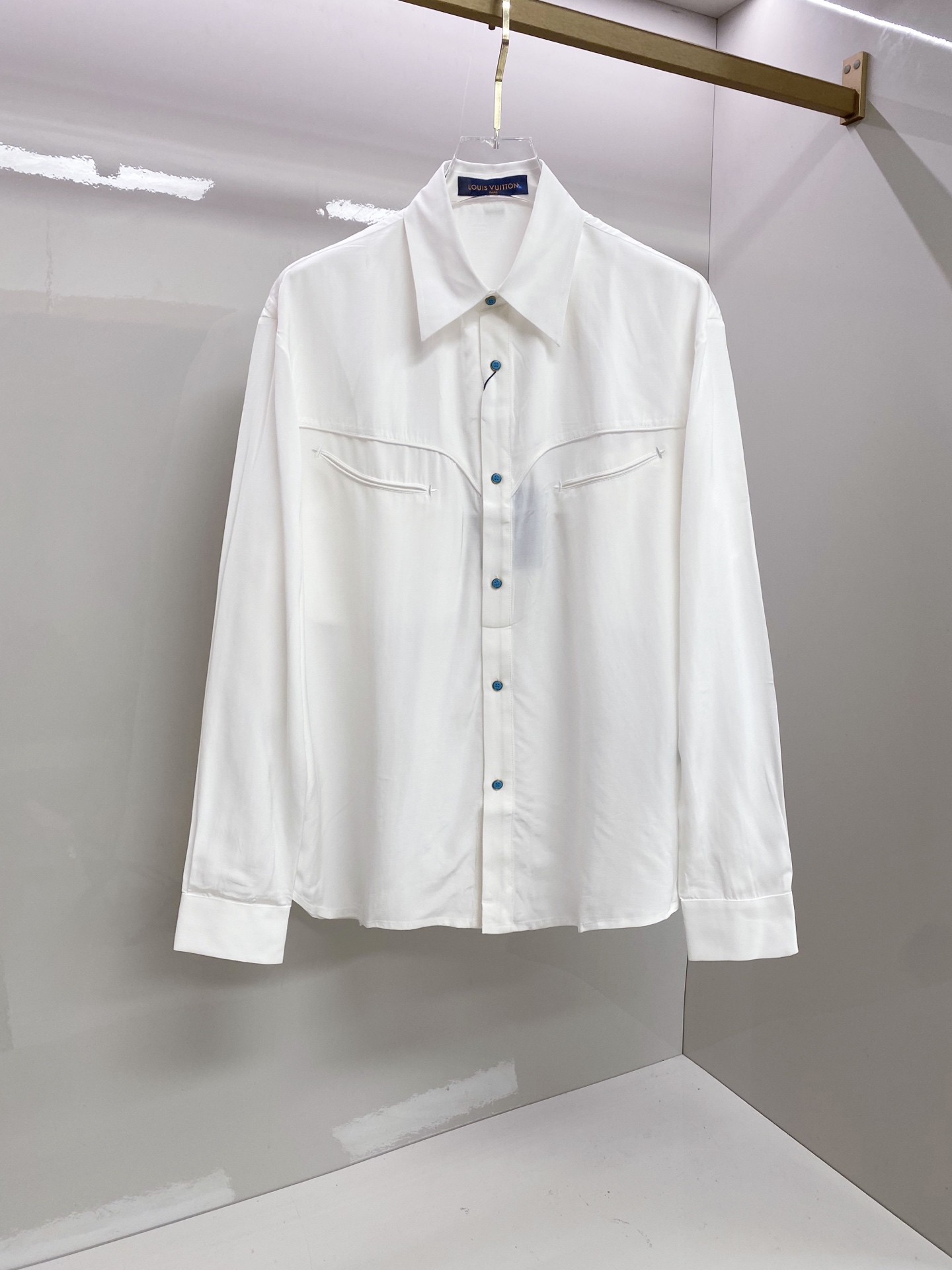 NO:835131,LV  The 2026ss spring and summer limited edition Western-style shirt reconstructs the classic white shirt aesthetic with neat tailoring and clever details. It is made of high-count and high-density poplin fabric, which feels silky and skin-friendly, has a soft light texture, and has a draped and stylish upper body; the body adopts the iconic arc of the Western shirt.  The bust line is divided and decorated with contrasting blue buttons to break the dullness. The curved shoulder design on the back echoes the blue button details on the cuffs. The neat straight silhouette is suitable for a variety of body shapes. Whether worn alone, layered or paired with a suit, it can easily create a relaxed, noble and high-end look.  Size 48-56,,louis vuitton,shirts,business suit,19860909LV 2026ss春夏限定西部风衬衫,以利落剪裁与细节巧思重构经典白衬衫美学.甄选高支高密府绸面料打造,触感丝滑亲肤,自带柔光质感,上身垂坠有型；衣身采用西部衬衫标志性的弧形胸线分割,搭配撞色蓝扣点缀,打破沉闷.后背弧形过肩设计与袖口蓝扣细节呼应,利落直筒版型适配多元身形,无论是单穿、叠穿还是搭配西装,都能轻松塑造松弛显贵的高级感穿搭. 码数48-56,,louis vuitton,shirts,business suit,,Men's clothing