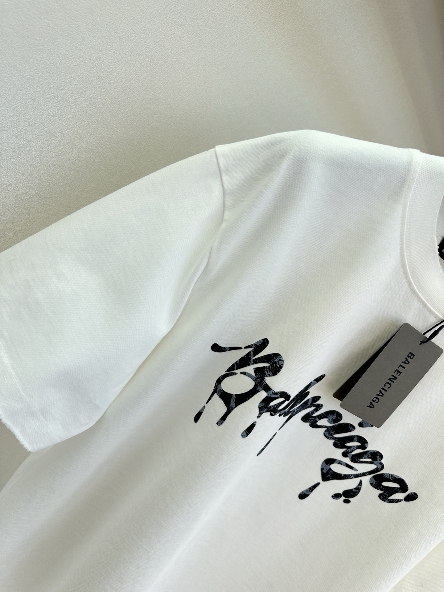 26S B家最新款 简约白T撞上暗黑风泼墨字母，随性又带着点酷感张力。毛边袖口弱化了规整感，松弛感拉满，