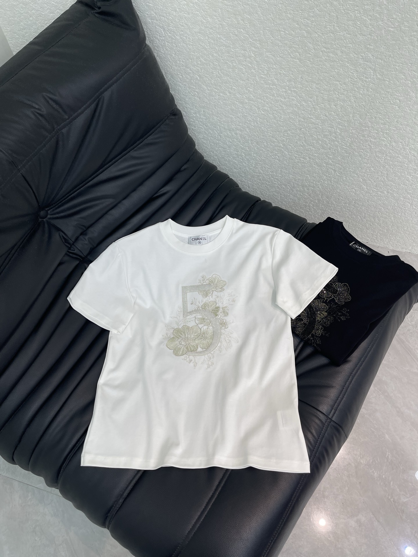 NO:806556,Chane*26 spring and summer new style right shoulder beaded No. 5 camellia short-sleeved T-shirt!  Customized mercerized cotton material, breathable and comfortable, full of texture, embroidered T-shirt cut, black and white high-end fashion, exquisite camellia beads and iconic digital embroidery on the chest, breaking the monotony of solid colors, and the delicate embroidery work shows the brand craftsmanship. The cotton fabric is soft and skin-friendly, and the regular version is slim and elegant. It is high-end when worn alone, or layered with a jacket to add layers. It is an all-purpose item that is indispensable in the wardrobe all year round!  SML AA,,chanel,jackets & coats,T-shirt,tees,t-shirt,19860909Chane*26春夏新款正肩钉珠5号山茶花短袖T恤！定制丝光全棉材质,透气舒适,质感十足,刺绣T恤剪裁,黑配白高级时尚,胸口精致的山茶花订珠和标志性数字刺绣,打破纯色单调,细腻的绣工尽显品牌工艺.全棉面料软弹亲肤,常规版型显瘦气质,单穿高级,叠穿外套更显层次,是衣橱里一年四季都少不了的万能单品！SML AA,,chanel,jackets & coats,T-shirt,tees，t-shirt,,Women's clothing