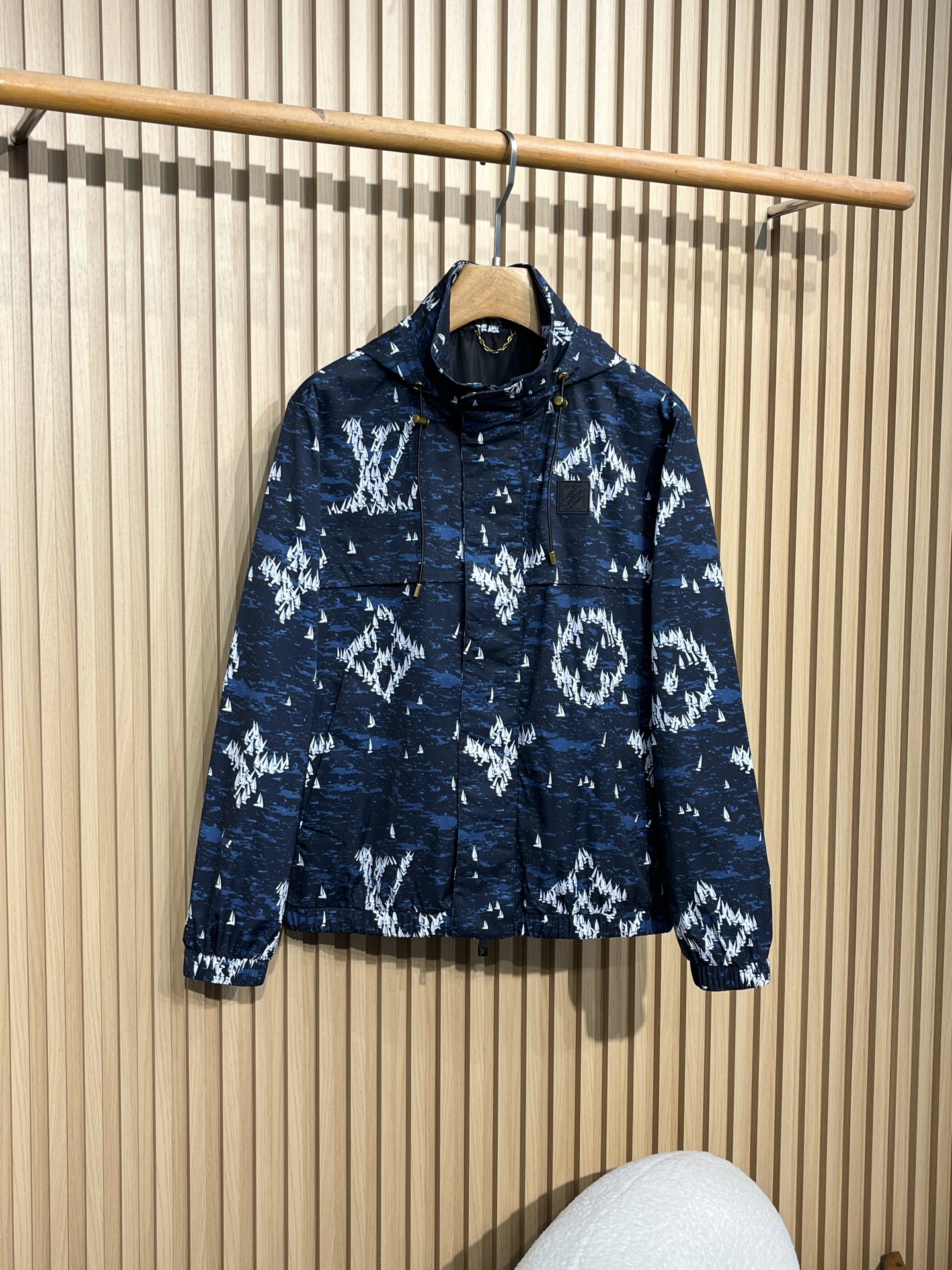 NO:507350,LOUIS VUITTON/Louis Vuitton Dark Blue Sailboat Printed Nylon Hooded Trench Coat Coat is made of dark blue as the background and is covered with white sailboat printing patterns, which combines fashion and uniqueness. The hooded design is casual and has certain wind and rainproof functions, and is suitable for wearing in various occasions. The hat is equipped with a drawstring, and the metal pendant at both ends of the drawstring is engraved with the words 'LOUIS VUITTON' to increase brand recognition. There is a black rubber sign on the left chest, with brand letter information imprinted on it, which is low-key and highlights the brand identity. The opening and closing of the clothes is combined with zippers and snaps to increase the firmness of the closure. The zipper head is designed with a simple design, and there are brand-related marks on the snaps. There is a larger pocket on the front to facilitate the placement of small items.  The cuffs and hem are elastic, which can effectively block the cold wind from entering, and are comfortable to wear and fit the body. The inner inner is black, the material is smooth, and the skin feels comfortable when worn. In some places, there is also a gold chain decoration. The main material of this windbreaker jacket is made of nylon, which is wear-resistant and windproof. It is not easy to pill or damage when worn. When it comes to light wind, it can also play a certain barrier role to keep the body dry. Size M-3XL M Shoulder width 46 Bust 110 Clothes length 65 L Shoulder width 47 Bust 114 Clothes length 66 XL Shoulder width 48 Bust 118 Clothes length 67 2X L Shoulder width 49 Bust 122 Clothes length 68 3XL Shoulder width 50 Bust 126 Clothes length 69,,louis vuitton,louis vuitton,jackets &  coats, hats, alexander wang19860909LOUIS VUITTON/路易威登 深蓝色帆船印花尼龙连帽风衣外套 以深蓝色为底色,布满白色帆船印花图案,兼具时尚感与独特性. 连帽设计,休闲且具有一定的防风防雨功能,适合多种场合穿着. 帽子配有抽绳,抽绳两端的金属坠饰上刻有“LOUIS VUITTON”字样,增添品牌辨识度. 左胸前位置设有一块黑色橡胶标识牌,上面压印着品牌字母信息,低调又彰显品牌身份. 衣服开合处采用拉链与按扣结合的方式,增加闭合的牢固性,拉链头设计简洁 ,按扣上也有品牌相关印记. 正面设有较大的口袋,方便放置随身小物品. 袖口和下摆处采用松紧设计,能有效阻挡寒风进入,穿着舒适且贴合身形. 内里为黑色,材质顺滑,穿着时皮肤触感舒适.在内里部分位置,还设有金色链条装饰 这款风衣外套主料采用锦纶,耐磨又防风,日常穿不容易起球、破损,遇到小风天气,也能起到一定阻隔作用,保持身体干爽. 尺码M-3XL M码肩宽46 胸围110 衣长65 L码肩宽47 胸围114 衣长66 XL码肩宽48 胸围118 衣长67 2X L码肩宽49 胸围122 衣长68 3XL码肩宽50 胸围126 衣长69,,louis vuitton,louis vuitton,jackets & coats,hats,alexander wang,Men's clothing