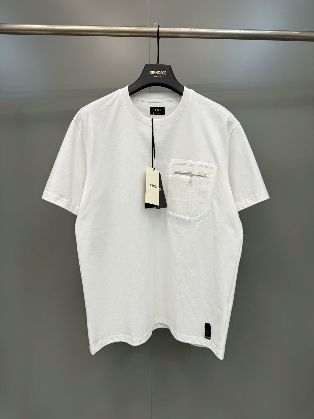 NO:830289,Cotton short-sleeved T-shirt with FD pocket zipper  Made of imported high-count pure cotton fabric, the texture is fine and soft, with excellent breathability and skin-friendly feeling. It is not easy to deform or turn yellow after long-term washing, and always maintains a crisp fit and refreshing wearing experience; classic round neck design, ribbed neckline processed with special technology  , moderately elastic and resistant to pulling, it fits the neck line while creating a clean and simple visual effect. The iconic chest pocket is made of different materials and is decorated with metal zippers embedded on the surface. The zipper teeth are fine and smooth, and the puller is thick and open and close.  Smooth, practical and stylish, it has become a low-key yet recognizable visual highlight; the overall tailoring of the garment is loose and moderate, and the dropped shoulder sleeves are suitable for a variety of body shapes. It can be worn alone or layered on a daily basis to create a relaxed and high-end atmosphere. The hem and cuffs are made of the same fabric hemming process, and the wiring is neat and fine, echoing the overall texture of the garment. The details show the brand's exquisite craftsmanship., Fendi - Clothing, fendi, T-shirt, tees, t-shirt,19860909FD口袋拉链装饰纯棉短袖T恤 采用进口高支纯棉面料,质地细腻柔软,兼具出色的透气性与亲肤感,久洗不易变形、泛黄,始终保持挺括版型与清爽穿着体验；经典圆领设计,罗纹领口经过特殊工艺处理,弹性适中且耐拉扯,贴合颈部线条的同时打造利落简约的视觉效果.胸前标志性口袋采用异材质拼接工艺,表面嵌入金属拉链装饰,拉链齿细密顺滑,拉头质感厚重且开合流畅,兼具实用性与造型感,成为低调又充满辨识度的视觉亮点；衣身整体剪裁宽松有度,落肩袖型适配多种身形,日常单穿或叠搭都能营造松弛高级的氛围感.下摆与袖口均采用同面料包边工艺,走线工整细密,与衣身整体质感形成呼应,细节处尽显品牌精湛工艺.,芬迪-服装,fendi,T-shirt,tees，t-shirt,,Women's clothing