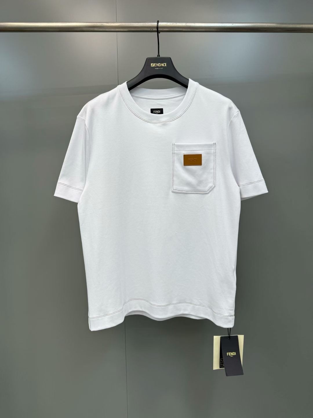 NO:855668,Fendi 26ss Fendi pocket leather label short sleeves are made of high-count combed cotton, 280g heavyweight double-ply jersey fabric, processed by pre-shrunk washing process.  The body adopts an Oversized drop shoulder version, the round neck is hemmed with natural fabric, and the collar is hemmed with double-needle stitching, combined with contrasting topstitching technology to strengthen the structural lines and improve durability. The front chest patch pocket is fixed with denim-style double topstitching technology, and the bag body is attached with an exclusive custom-made molded leather tag, which is presented with the brand logo using a press process. The bag mouth and bottom are reinforced with dates, and the details highlight the hard-core texture of workwear style.  Size s-XL, Fendi-clothing, fendi, fendi, versace, T-shirt,19860909Fendi 26ss 芬迪口袋皮标短袖 采用高支精梳棉为原料,280g重磅双股平纹针织面料,经预缩水洗工艺处理, 衣身采用Oversized落肩版型,圆领采用本布包边工艺,领口采用双针冚线锁边,结合撞色明线辑边工艺,强化结构线条的同时提升耐用性.前胸贴袋采用牛仔式双明线工艺固定,袋身附专属定制开模皮牌,以压烫工艺呈现品牌标识,袋口与袋底采用打枣加固工艺,细节处彰显工装风格的硬核质感 尺码s-XL,芬迪-服装,fendi,fendi,versace,T-shirt,,Women's clothing