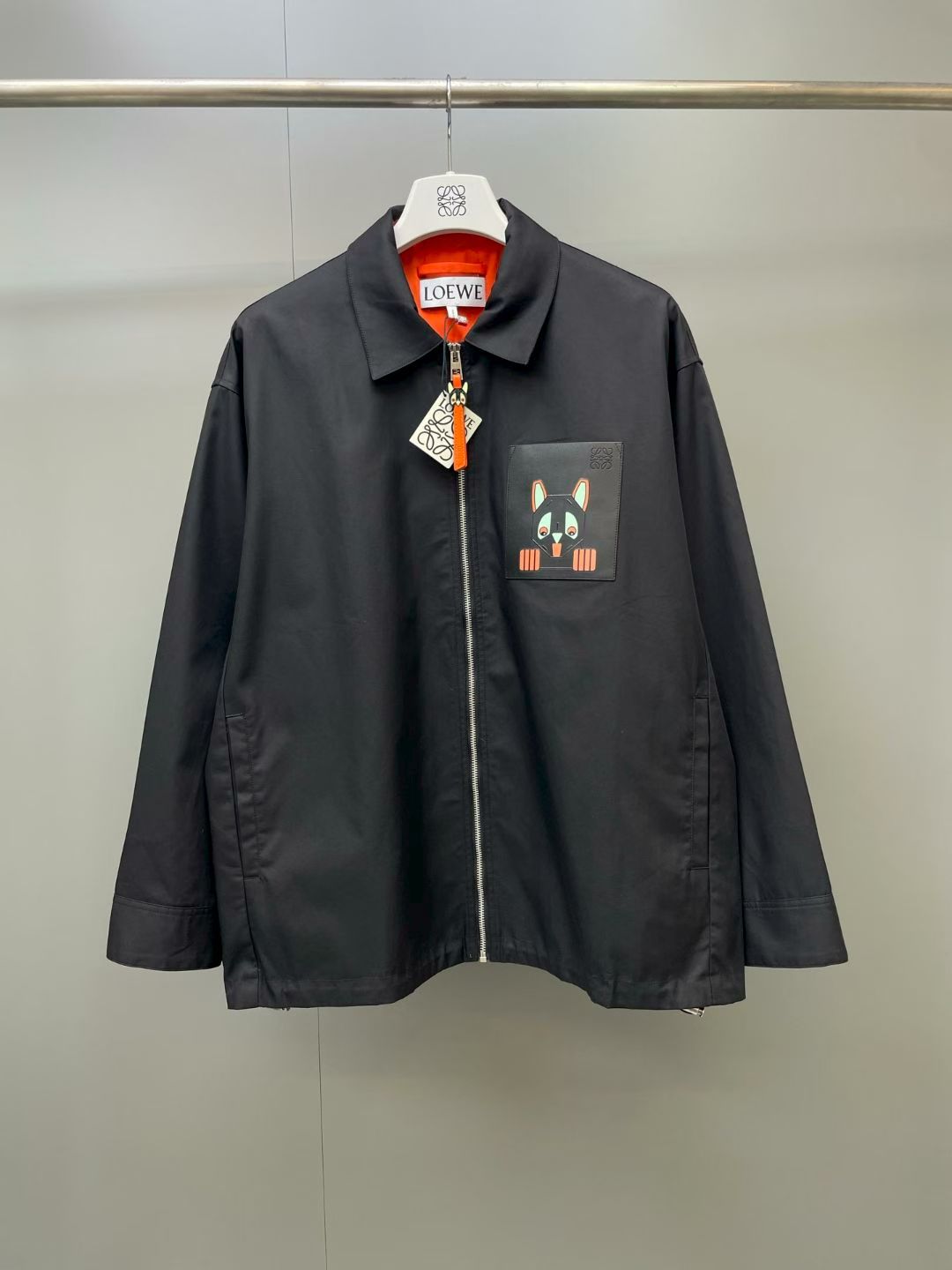 NO:867992,LO artist co-branded cartoon patch lapel work jacket  It is made of customized high-density anti-wrinkle twill woven fabric, which has been treated with liquid ammonia shaping and three-proof coating. The surface of the fabric is smooth and neat, with a delicate matte texture. It feels crisp and not easy to collapse and deform. The fabric is both windproof, water-repellent and breathable. It is not easy for fine rain and snow to soak into the body. It has outstanding practicality in daily commuting against the cool evening breeze, and the inner matching is eye-catching.  The contrasting orange-red cotton lining feels skin-friendly and smooth to put on and take off without snagging; the body adopts a classic small lapel cut, and the double-needle seam on the collar is neatly turned, which can stand up naturally to modify the neck line, taking into account both styling and windproof effect; the placket is equipped with a customized metal zipper, the zipper teeth have been precision polished to pull smoothly without snagging, and the zipper head has a cartoon shape  For decoration, the zipper tape is made of the same orange-red fabric as the lining, and the color matching of the details echoes the interior design; the body is made of a loose shoulder workwear style, with moderately widened length and sleeve allowance, so that the arms can be lifted without restraint. It can be worn with a sweatshirt and sweater, giving a high degree of freedom in layering and matching; the cuffs are made with flat seams and tight seams, and the stitching is solid and secure, and the hem has hidden invisible drawstrings  The rope design can be tightened as needed to shape the waist shape, allowing you to wear two styles in one garment; the entire garment adopts dense overlocking technology in many places, and the internal wiring is clean and regular to eliminate excess threads. The exquisite details highlight the light and luxurious workmanship., Loewe-clothing, loewe, hoodie, sweatshirts, jackets  & coats,19860909LO艺术家联名卡通贴布翻领工装夹克 采用定制高密抗皱斜纹梭织面料,经过液氨定型与三防涂层工艺处理,面料表层平整利落,自带细腻哑光质感,触感挺括不易软塌变形；面料兼具防风抗泼水与透气属性,细碎雨雪不易浸润衣身,日常通勤抵御微凉晚风实用性出众,内里搭配亮眼撞色橙红全棉里布,触感亲肤顺滑,穿脱顺滑不勾丝；衣身采用经典小翻领剪裁,领面双针锁边车工工整,可自然立起修饰脖颈线条,兼顾造型感与防风效果；门襟配备定制金属拉链,拉链齿经过精密打磨处理拉动顺滑无卡顿,拉链头搭配卡通造型装饰,拉链布带选用同内里橙红色面料,细节配色呼应内里设计；衣身选用宽松落肩工装版型,适度放宽衣长与袖管余量,手臂抬举毫无束缚,可内搭卫衣针织衫,叠穿搭配自由度极高；袖口采用平整收口密缝工艺,锁线扎实牢靠,下摆暗藏隐形抽绳设计,可按需收紧塑造收腰版型,一衣穿出两种穿搭风格；整件成衣多处采用密拷锁边工艺,内里走线干净规整,杜绝多余线头,细节考究凸显轻奢做工.,罗意威-服装,loewe,hoodie,sweatshirts,jackets & coats,,Women's clothing