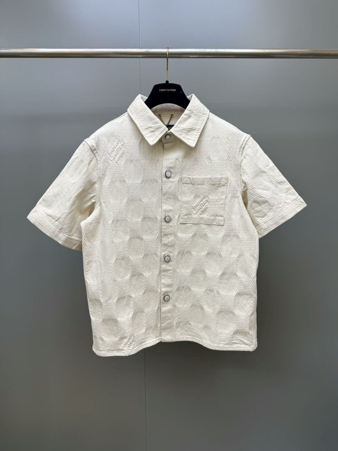 NO:899974,1V 26ss 3D checkered denim half-sleeve off-white 3D Damier jacquard fabric, showing Pharrell Williams in 2026  The new silhouette launched in the spring and summer show. The rounded collarless design and buttoned cuffs embody the dandy style of the season and go well with the same style of trousers. Yarn-dyed jacquard denim refers to a type of denim made using the yarn-dyed jacquard process, which is a twill weave and indigo-dyed denim. This kind of fabric uses the yarn-dyed jacquard process to directly weave various patterns and patterns into the weaving process, making the surface of the denim show a richer texture and visual effect.  Sand washing of finished pieces is a post-treatment process for jeans, which makes the clothes have a certain fading effect and old feeling after washing. During the sand washing process, the clothes will be rubbed with pumice or sand in a special sand washing machine to produce a uniform layer of plush on the surface of the fabric, giving the denim a special texture and feel. Collarless Cow  The characteristic of the denim shirt is that it does not have a traditional collar design and uses buttons as a closure method to create a relaxed and casual feeling. The curved hem denim shirt is a unique design with a curved hem, making the entire shirt more visually dynamic and streamlined. Louis Vuitton-clothing, Louis  vuitton,jeans,shirts,198609091V 26ss 3D方格牛仔半袖米白 3D Damier 提花面料,展现 Pharrell Williams 于2026 春夏秀场推出的崭新廓形.圆润无领设计和系扣袖口凝聚当季丹迪风采,与同款长裤搭配相宜.色织提花丹宁是指一种采用色织提花工艺制作的牛仔布,也就是斜纹织法的、靛蓝染色的粗斜纹布.这种布料通过色织提花工艺,在织布过程中直接织入各种花纹和图案,使得牛仔布表面呈现出更加丰富的纹理和视觉效果. 成件砂洗是一种牛仔裤的后处理工艺,使衣物在洗后具有一定的褪色效果和陈旧感.砂洗过程中,衣物会与浮石或专用砂洗机中的砂粒进行摩使织物表面产生一层均匀的毛绒,赋予牛仔擦,但布特殊的质地和手感.无领牛仔衬衫它的特点是没有传统的领子设计,采用纽扣作为闭合方式,打造轻松随意的感觉.弧形下摆牛仔衬衫是一种设计独特、摆呈现出弧形的设计,使得整件衬衫在视觉上更具动感和流线感.,路易威登-服装,louis vuitton,jeans,shirts,,Women's clothing