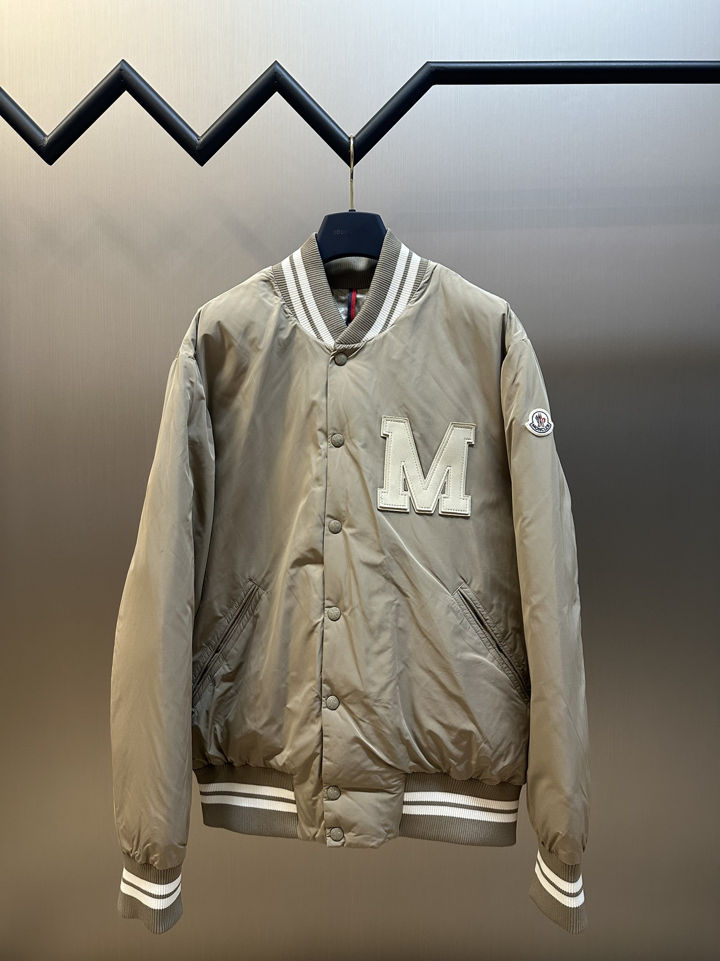 Moncler 学院风夹克羽绒服 学院风格与经典棒球夹克的融合，蒙口Lateltin羽绒服汲取了学院风格的经典元素，同时结合棒球夹克的经典造型，使得整款羽绒服既具有复古韵味 又不失现代时尚感。 标识与字母组合贴片刺绣，在羽绒夹克上饰有蒙口…