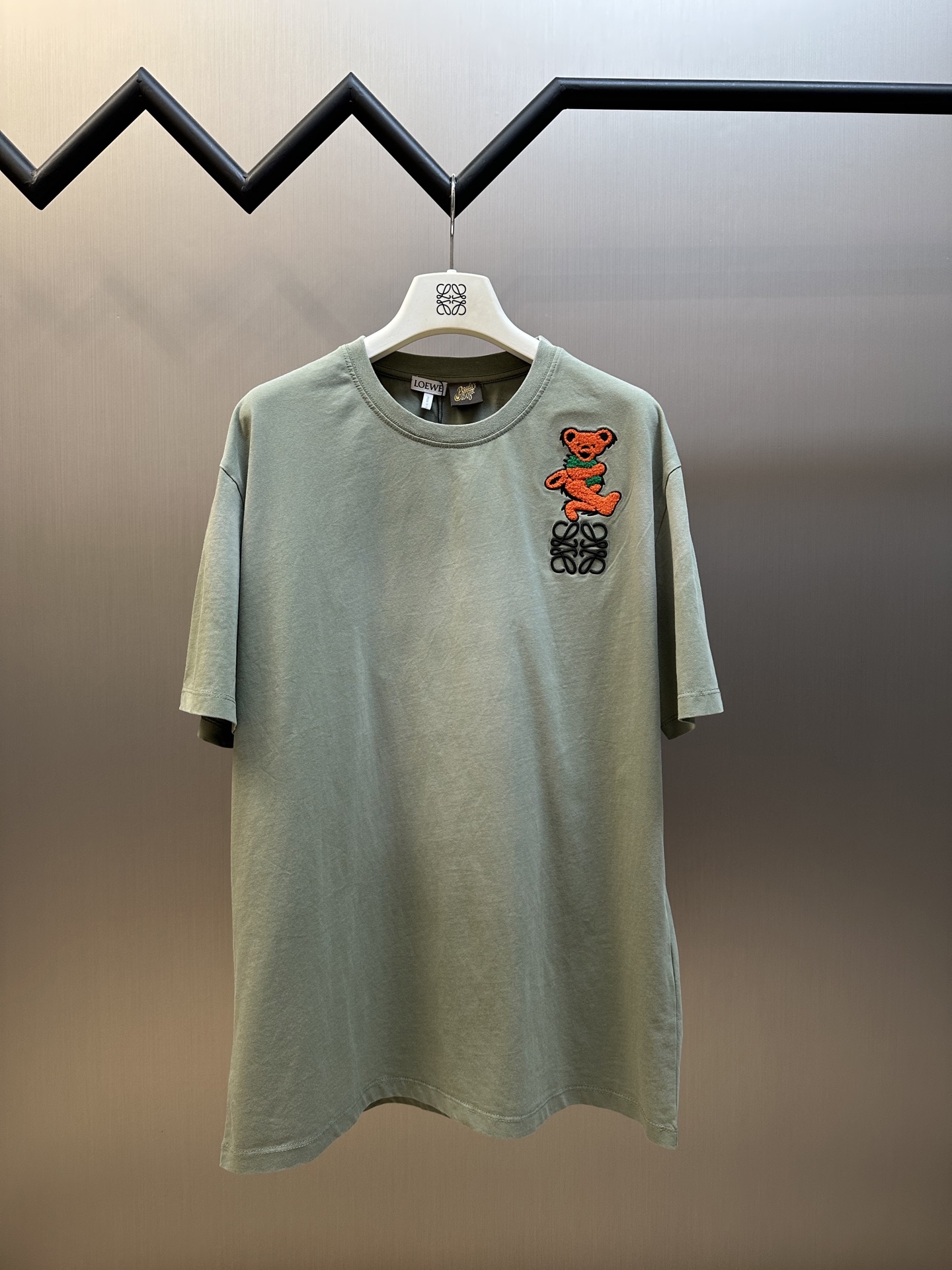 NO:414867,LOEWE Dancing Bear Embroidered Short Sleeve Lightweight Pure Cotton Fit fabric, using 24S special textile tight cotton, 185g; matched with 32S1X1 tie-frame thread, 220g. Due to the relatively thin 24 yarns, the fabric may feel very soft, the texture is light and highly breathable. Through the special textile process, the fabric has a unique texture and appearance; the tight structure makes the fabric more wear-resistant and wrinkle-resistant, and can maintain its beauty and smoothness for a long time.  The chest is decorated with bear terry cloth embroidery, and the corresponding color and thickness are used to choose embroidery threads suitable for the color and thickness of the embroidery; the embroidered terry cloth must be delicate in the material and moderate in the thickness to ensure the embroidery effect and feel. During the embroidery process, the strength must be controlled to avoid excessive force causing wrinkles or damage to the terry cloth; at the same time, the continuity and smoothness of the lines are maintained. The final treatment is made with scissors to trim off the excess thread and burrs to make the lines more neat. The logo embroidery uses three-dimensional embroidery technology, and the letters clearly restore the spacing curve. Select mercerized embroidery threads with glossy sense, and the machine combines complex embroidery needlework and fine detail processing to create the embroidery effect of three-dimensional relief. Classic trademark letter design, the embroidery is finely stitched, the font is clear and the line feel is strong.  After the garment is fried sand and made by old craftsmanship, the garment is fried and made by old craftsmanship. The garment is dyed and dyed and washed with water. The fabric is dyed and processed by stone milling. The garment is constantly immersed in the dye and rolls. After the garment is fried, the fabric is slightly faded, and the color of the original fabric is changed to show nostalgic colors of different shades and light and dark. Simple vertical round neck short-sleeved version, the paper pattern is developed with minimal body cut, knitted material has certain extension performance, and the upper body will not be tightly tied. The round neck is the same color ribbed splicing collar, and the inner sticking process of the back neck effectively prevents the neckline deformation after multiple washes, fit shoulder lines, bottom swing and cuffs, and the edges of the special machine knight and car. sizexs s m l,,loewe,T-shirt,alexander wang19860909LOEWE 跳舞熊绣花短袖 轻质纯棉紧密棉面料,采用24S特纺织紧密棉,185g；搭配32S1X1拉架螺纹,220g.由于采用了相对较细的24支纱线,面料的手感可能非常柔软,质地轻薄并有高度透气性.通过特纺工艺,面料具有独特的纹理和外观；紧密的结构使得面料更加耐磨、抗皱,能够保持较长时间的美观和平整. 胸前饰有小熊毛巾布刺绣,对版对色选用适合相应颜色和粗细的刺绣线；刺绣的毛巾布要求材质细腻,厚度适中,保证刺绣效果和手感选择.在绣花过程中,要控制好力度,避免力度过大导致毛巾布起皱或损坏；同时保持线条的连续性和流畅性.后整处理用剪刀修剪掉多余的线和毛刺,使线条更加整洁. 标志徽标刺绣,采用立体刺绣工艺,字母清晰还原间距曲线.精选具有光泽感的丝光绣线进行,机结合复杂刺绣针艺,精细的细节处理,造就了立体浮雕的刺绣效果.经典商标字母设计,刺绣精细针法绵密,字体清晰且线条感和立体感强. 成衣后炒砂做旧工艺,成衣后进行炒色工艺制作而成,成衣环保新工艺转染染色、洗水做旧.通过石磨的方式对面料进行染色加工,成衣不断地浸入染料中翻滚.炒砂后面料轻微掉色效果,改变原面料颜色呈现出深浅一明暗不同的怀旧色彩. 简约垂直圆领短袖版型,对版纸样开发极简直身剪裁,针织材质具有一定延展性能,上身不会紧紧束身.圆领同色罗纹拼接领口,后领口内贴条工艺,有效防止多次穿洗后领口变形,合身肩线,底摆与袖口专机坎车明线收边. sizexs s m l,,loewe,T-shirt,alexander wang,Men's clothing