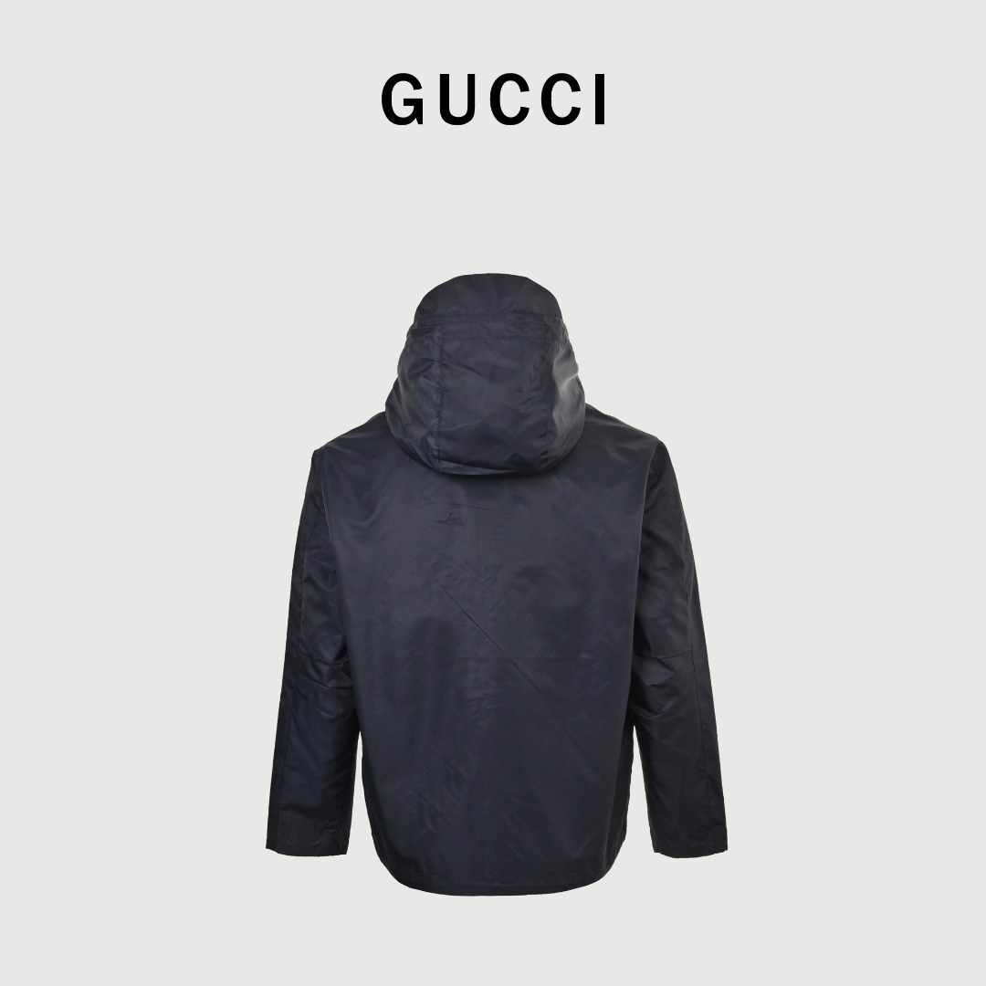 GUCCI古驰GUC 斜纹尼龙防风领连帽外套 选用100%锦纶纤维紧密编织而成的蓝色密织斜纹尼龙面料.经纬纱线之间的空隙非常小,表面呈现清晰的45度角斜向纹理.锦纶突出的耐磨性,抗拉扯等优点使成衣增加使用寿命.较小的密度强化防风性,同时兼具一定的防水性能,在室外能更好的发挥其功能性. LOGO刺绣贴饰采用0.3毫米超细聚酯绣线,经激光切割定型工艺打造浮雕质感.每片贴饰经过5道抗皱处理,确保水洗后仍保持原有形态. False Two-Piece设计增添层次感和独特性,采用高端隐形暗扣将帽子部分和大身链接一体,独立完整的双层结构,单穿叠穿皆宜.定制辅料
