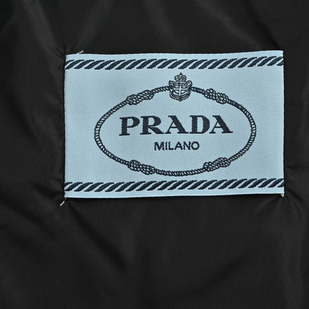 本地自取 💰580 Prada/普拉达 25Fw 三角标立领绗缝羽绒服 PRADA饰三角标立领羽绒夹克，甄选高支府绸面料，经纱细密、纬纱粗韧的高密编织造就独特哑光十字肌理，兼具棉质亲肤与尼龙挺括质感；内填230g 90精选白鸭绒，蓬松回弹且轻盈保暖。创新采用65度斜线绗缝工艺，分区独立线迹赋予面料充足形变空间，不易绷紧断裂，菱形网格更添现代高级动感；袖口与下摆搭配弹力罗纹设计，柔软贴合锁温无束缚，辅以一比一定制三角标、拉链头及纽扣，尽显品质细节。 Size:46-52