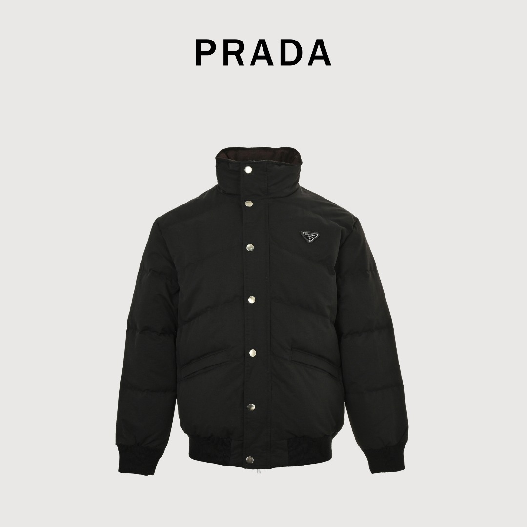本地自取 💰580 Prada/普拉达 25Fw 三角标立领绗缝羽绒服 PRADA饰三角标立领羽绒夹克，甄选高支府绸面料，经纱细密、纬纱粗韧的高密编织造就独特哑光十字肌理，兼具棉质亲肤与尼龙挺括质感；内填230g 90精选白鸭绒，蓬松回弹且轻盈保暖。创新采用65度斜线绗缝工艺，分区独立线迹赋予面料充足形变空间，不易绷紧断裂，菱形网格更添现代高级动感；袖口与下摆搭配弹力罗纹设计，柔软贴合锁温无束缚，辅以一比一定制三角标、拉链头及纽扣，尽显品质细节。 Size:46-52