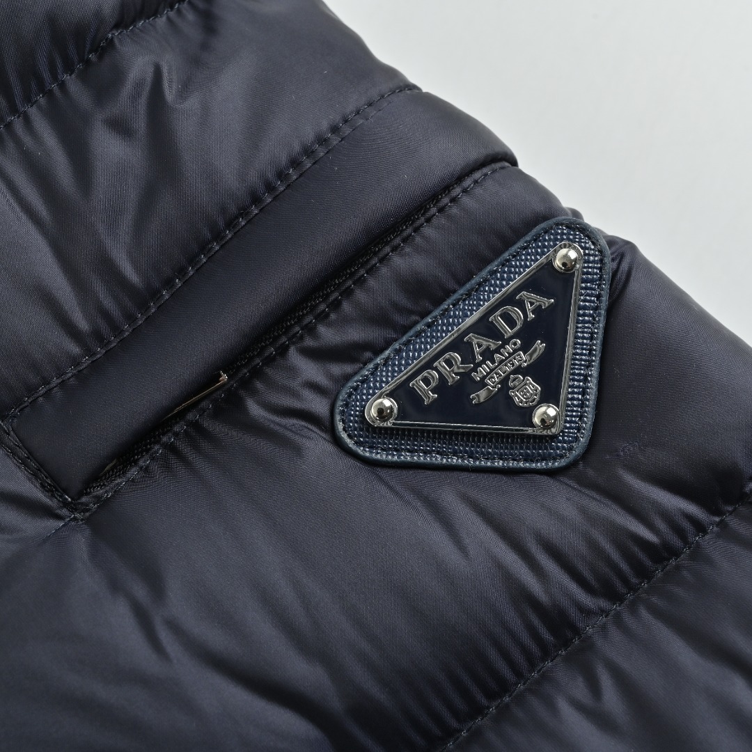 本地自取 💰650
Prada/普拉达 25Fw手臂三角标口袋立领羽绒服
采用新国标90白鸭绒填充，顶级版本，区分市面通货，男女同款全新美学灵感趣味设计,渠道性质精品。让整体造型设计更加优雅时尚，今夏最火系列，无数明星潮人追捧。裁剪工艺细节处理工整为玩味时尚增添色彩!工整细致，合身的版型构造更是独具匠心，上身不仅有着出彩的辨识度更是减龄青春。一款穿着意义还有穿搭性能都很极致的款式，绚丽的色系调配，此款的工艺必然也是极致非凡，上身的舒适度绝对足够的强大，也是奢品本质的一种彰显！柔软轻薄，触感更是极端撩人，透气性能十分之强大，尤为适合春夏季节的穿搭所需，妥妥的穿着享受，并且各处的细节以及织带的工艺都是尽善尽美，更显高级感！ 
颜色：黑色、藏青
编码：8026
尺码：48-56