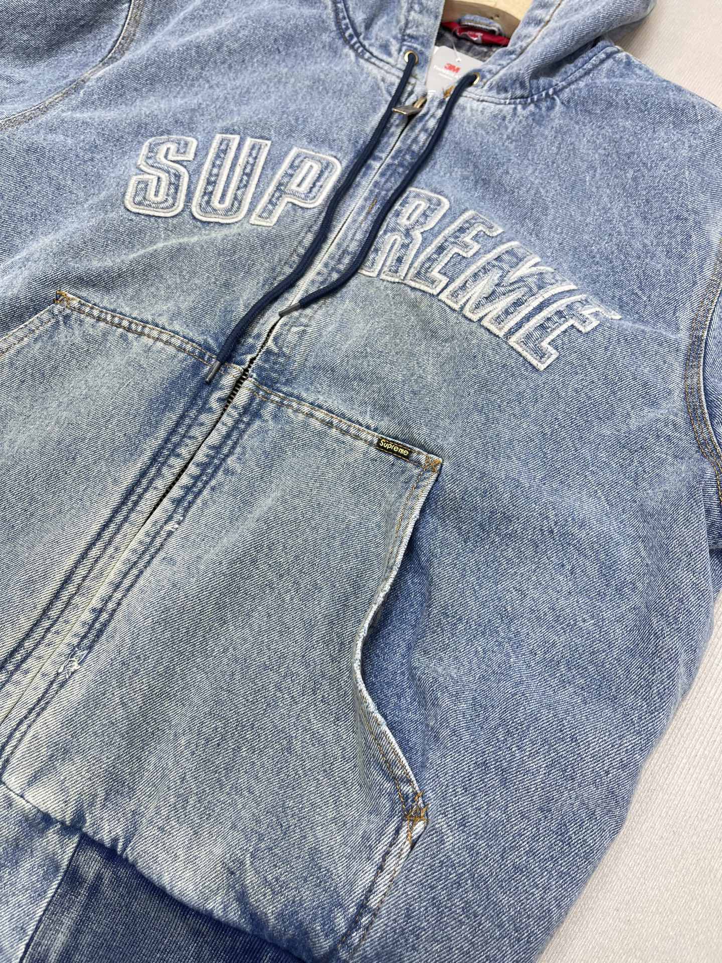 💰460🔥Supreme FW25 WEEK1 Reflective Arc Hooded Work Jacket 反光徽标字母拉链开合连帽工装夹克棉服外套 男女同款
全单宁牛仔面料 绗缝棉法兰绒里衬。正面下方有大口袋，内部胸袋。针织罗纹袖口和下摆。正面有3M®反光与字母徽标贴花。内里格子布千米起订  上身很好看的秋冬新款
颜色：水洗蓝 水洗黑色
尺码：S M L XL
         肩宽    衣长  胸围    袖长
S        58       68     136    66
M       60       70     140    67
L        61       72      144    68
XL      62       74      148    69