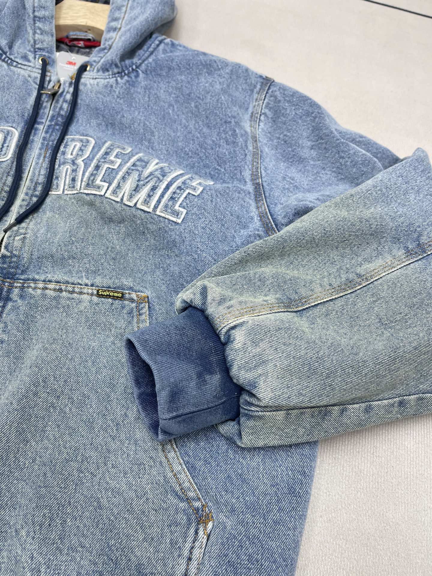 💰460🔥Supreme FW25 WEEK1 Reflective Arc Hooded Work Jacket 反光徽标字母拉链开合连帽工装夹克棉服外套 男女同款
全单宁牛仔面料 绗缝棉法兰绒里衬。正面下方有大口袋，内部胸袋。针织罗纹袖口和下摆。正面有3M®反光与字母徽标贴花。内里格子布千米起订  上身很好看的秋冬新款
颜色：水洗蓝 水洗黑色
尺码：S M L XL
         肩宽    衣长  胸围    袖长
S        58       68     136    66
M       60       70     140    67
L        61       72      144    68
XL      62       74      148    69