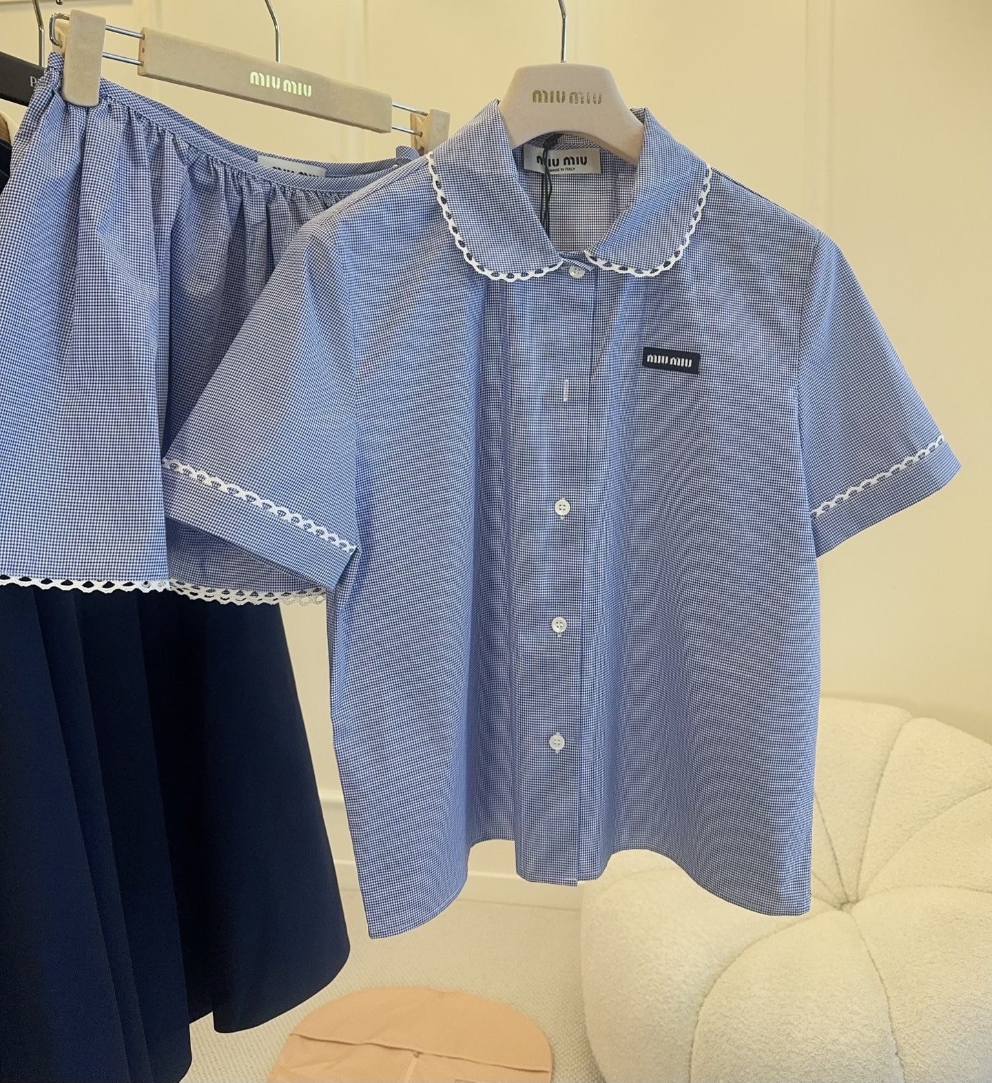 NO:801219,Shirt Skirt Miu Miu  2026 new blue plaid college-style suit, including short-sleeved shirt + mini skirt. Light blue base with white fine plaid, white embroidered lace on the collar and cuffs, and a black logo on the chest that is very recognizable. Cotton poplin fabric, soft and comfortable, slim and straight fit. Skirt lace-up design + lace edges, full of girly feel, perfect for daily commuting, dating, and taking photos. The blue and white color scheme is fresh and reduces age, full of college-style atmosphere, and you can easily get youthful vitality!  ,,miumiu,skirts,shirts,T-shirt,19860909衬衫 半裙Miu Miu 2026新款蓝色格纹学院风套装,包含短袖衬衫+迷你半身裙.浅蓝底配白色细格纹,领口和袖口有白色刺绣花边,胸前黑色徽标超有辨识度.棉质府绸面料,柔软舒适,修身直筒版型.半身裙系带设计+蕾丝边,少女感满满,日常通勤、约会、拍照都很出片.蓝白配色清新减龄,学院风氛围感拉满,青春活力轻松get！,,miumiu,skirts,shirts,T-shirt,,Women's clothing