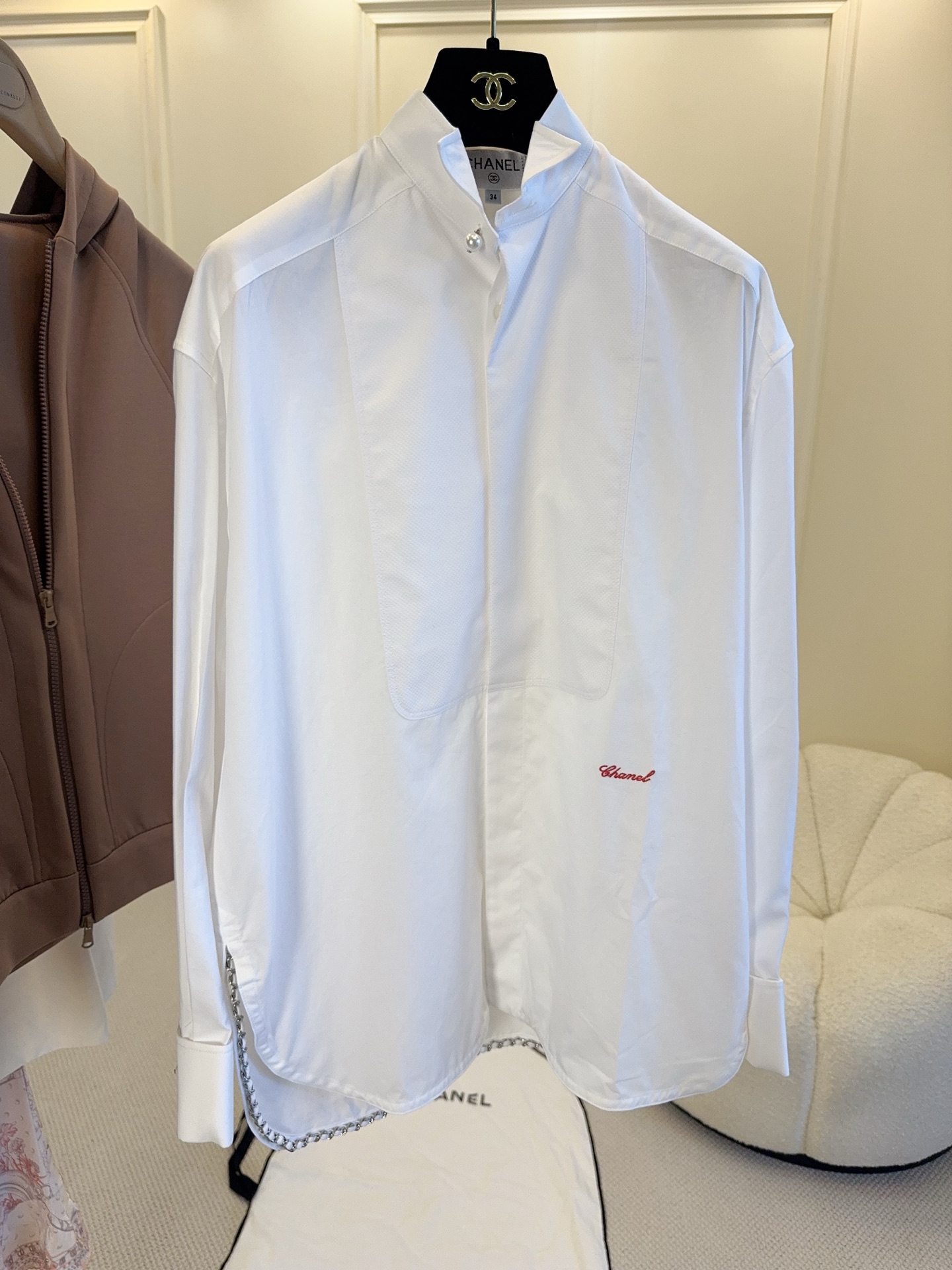 NO:886461,Chanel 2026 West Gate Chain White Shirt is a 2026 spring and summer series designed by Matthieu Blazy. It has a loose Oversize version, classic white cotton fabric, and a metal chain sewn on the hem. The details are perfect!  Pearl lapel + red embroidery, elegant and fashionable, the chain design is very recognizable, it makes a sound when walking, and full of aura. It can be easily used for commuting, dating, and daily life. It goes well with trousers or skirts. It is a high-end item that is practical and has a sense of design!  ,,chanel,versace,skirts,shirts,19860909Chanel 2026西门口链条白衬衫,是Matthieu Blazy设计的2026春夏系列,宽松Oversize版型,经典白色棉质面料,衣摆缝有金属链条,细节满分！珍珠翻领+红色刺绣,优雅又时髦,链条设计超有辨识度,走路自带声响,气场全开.通勤、约会、日常都能轻松驾驭,搭配裤装或裙装都很出彩,是实用又有设计感的高端单品！,,chanel,versace,skirts,shirts,,Women's clothing