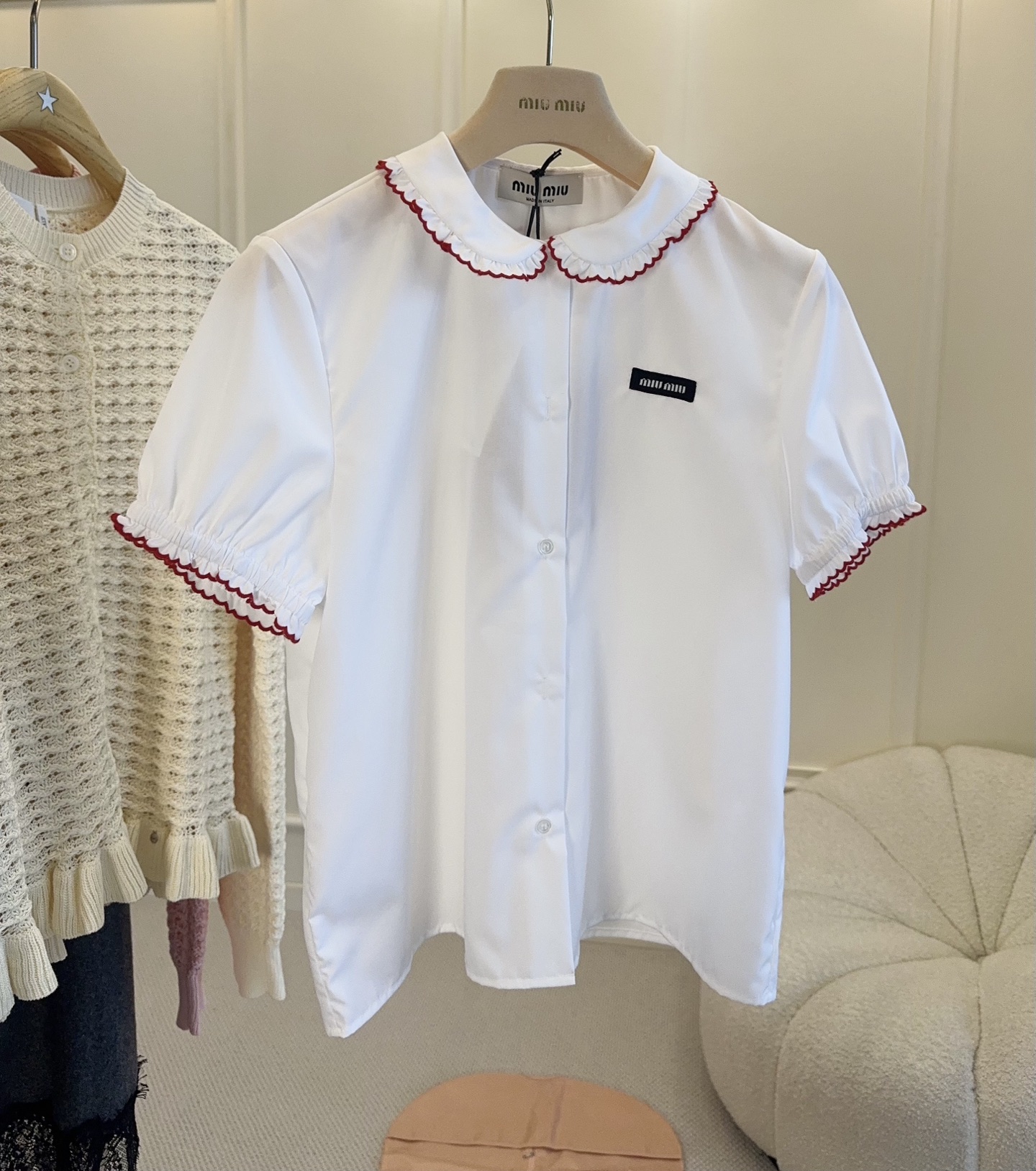 NO:891142,Miu Miu 2026 new baby collar white shirt, made of lightweight and breathable cotton fabric, embellished with red ruffles, full of sweet retro girly feel. Short sleeves + brand logo on the chest, exquisite details, full of college style. It can be easily used for daily commuting and dating. Pair it with a pleated skirt or high-waisted pants, and you can easily get a girly look!  ,,miumiu,skirts,shirts,T-shirt,19860909Miu Miu 2026新款娃娃领白衬衫,棉质面料轻薄透气,红色荷叶边点缀,甜美复古少女感满满.短袖+胸前品牌标识,细节精致,学院风十足.日常通勤、约会都能轻松驾驭,搭配百褶裙或高腰裤,元气少女感轻松get！,,miumiu,skirts,shirts,T-shirt,,Women's clothing