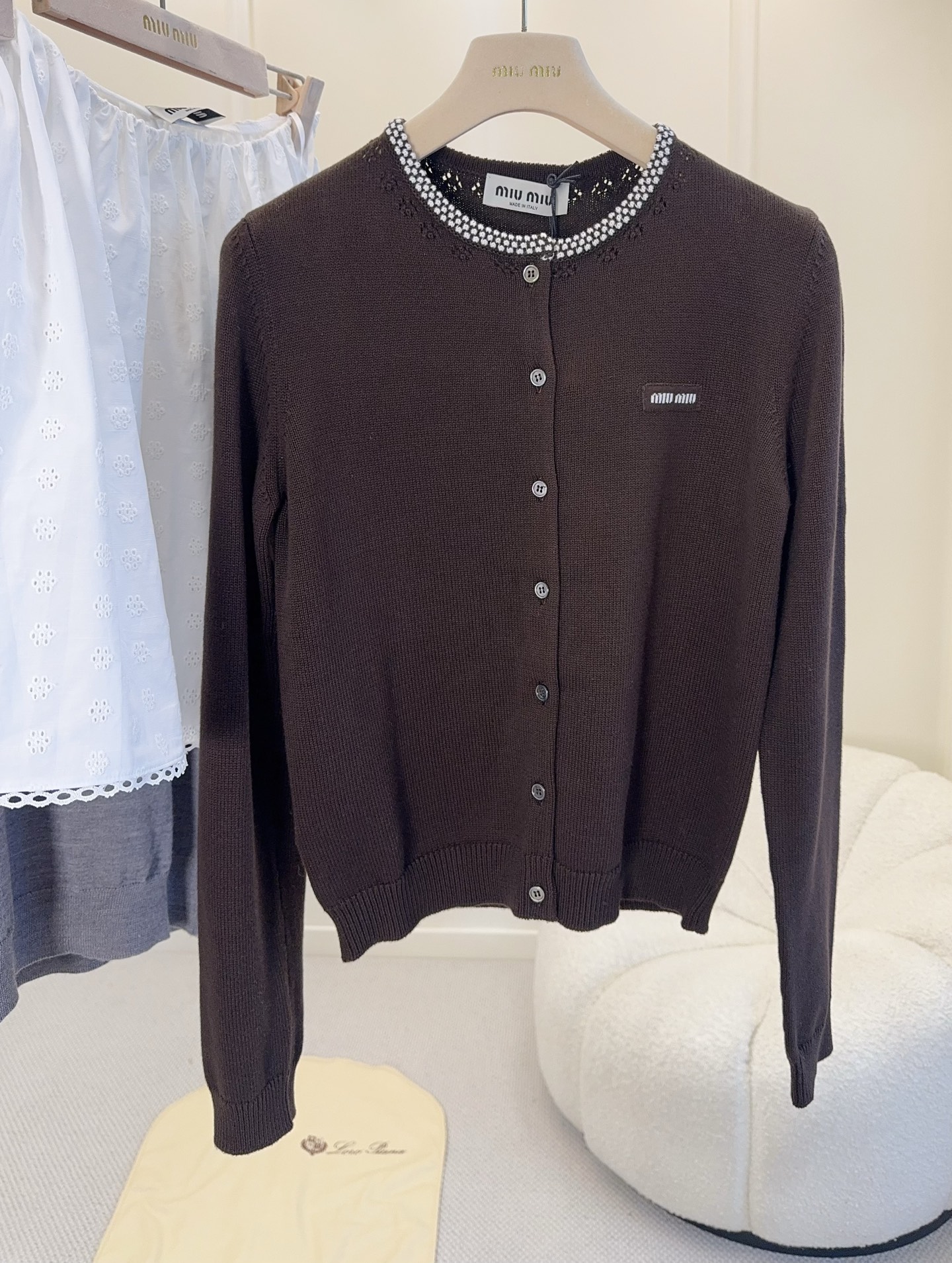 NO:952167,miumiu2026 Early Autumn Maillard Brown Round Neck Knitted Cardigan, a new classic college style cardigan, Maillard chocolate color is really high-end, filling the atmosphere of early autumn, combed fine pure cotton yarn, dyed dark brown color is gentle and white, imported machine creates a clean and smooth texture, regular round neck cardigan version, half raglan sleeve design super hidden flesh  , the cutout holes on the neckline + the white contrasting intarsia decoration are so exquisite, instantly enhancing the sense of sophistication. The classic logo on the chest highlights the fashionable atmosphere, low-key and texture ~ The shape is crisp and not soft, it is very suitable for layering or wearing alone in early autumn ~ It is very suitable to be paired with a series of miu jeans and skirts. It is a must-have for Miu girls' early autumn wardrobe!  ,,miumiu,skirts,jeans,19860909miumiu2026早秋美拉德棕色圆领针织开衫,经典学院风开衫新品,美拉德巧克力色真的好高级,把早秋氛围感拉满,精梳细腻纯棉纱线,定染深咖色温柔又显白,进口机打造干净平整织面质感十足,常规圆领开襟衫版型,半插肩袖设计超级藏肉,领口的挑孔镂空+白色撞色嵌花装饰太精致了,瞬间提升精致感,胸口饰经典logo徽标凸显时髦气息,低调又有质感~版型挺括不软榻,早秋叠穿、单穿都超合适~下面搭配miu一系列牛仔裤、半身裙都超合适,是Miu女孩早秋衣橱的必备款！,,miumiu,skirts,jeans,,Women's clothing