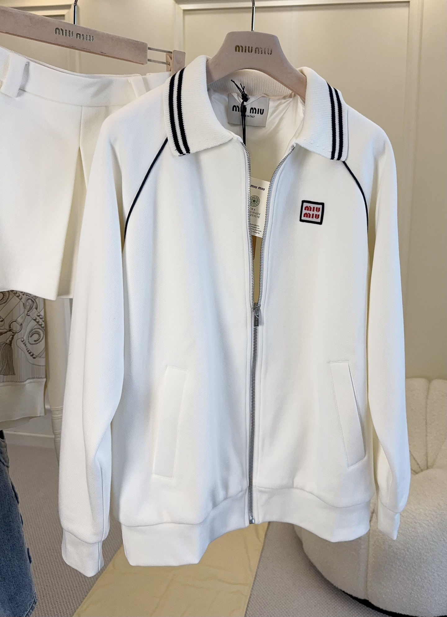 NO:954782,Jacket, skirt, Miu Miu 2026 new classic college suit | Girly feeling never goes out of style. Who can resist miumiu’s atmospheric tennis girl outfit!  Cream white polo lapel jacket, contrasting black and white stripes on the collar, exquisite small square mark embroidery, full of recognition. The zippered cardigan has a neat and slim fit, with raglan sleeves that are not flattering on the figure, and can be relaxed for daily use. The matching pleated skirt has a hidden culottes design, which is full of security. The navy contrast stripes on the hem echo the top. Pure off-white and soft, not picky, soft and waxy piqué fabric is comfortable and breathable. Retro tennis college style, suitable for commuting, dating, and traveling straight out.  It has the elegant gene of its own brand, is simple and not exaggerated, and the upper body looks like a wealthy lady. The complete set saves you the trouble of dressing, and you can easily wear it to create a pure and smart girly temperament!  ,,miumiu,skirts,jackets & coats,19860909外套 半裙Miu Miu2026新款经典学院套装｜少女感永不过时谁能拒绝miumiu自带氛围感的网球少女穿搭！奶白polo翻领外套,领口黑白条纹撞色,精致小方标刺绣,辨识度拉满.拉链开衫版型利落显瘦,插肩袖不挑身材,日常松弛感拿捏.配套百褶短裙暗藏裤裙设计,安全感十足,下摆藏青撞色条纹呼应上衣.纯正米白柔和不挑皮,软糯珠地面料舒适透气. 复古网球学院风,通勤、约会、出游一套直接出门. 自带品牌优雅基因,简约不浮夸,上身就是千金大小姐既视感.成套搭配省去穿搭烦恼,轻松穿出清纯灵动的少女气质！,,miumiu,skirts,jackets & coats,,Women's clothing