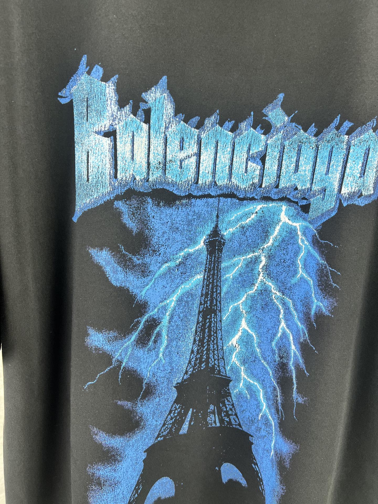 Balenciaga BALENCI*GA 铁塔闪电印花T恤 本品采用重磅精梳纯棉面料经预缩水处理 触感厚实挺括 宽松落肩版型贴合街头潮流风格 兼顾舒适与造型感 正面印花采用胶印结合做旧磨边工艺 先以高饱和度油墨还原蓝色闪电与埃菲尔铁塔轮廓