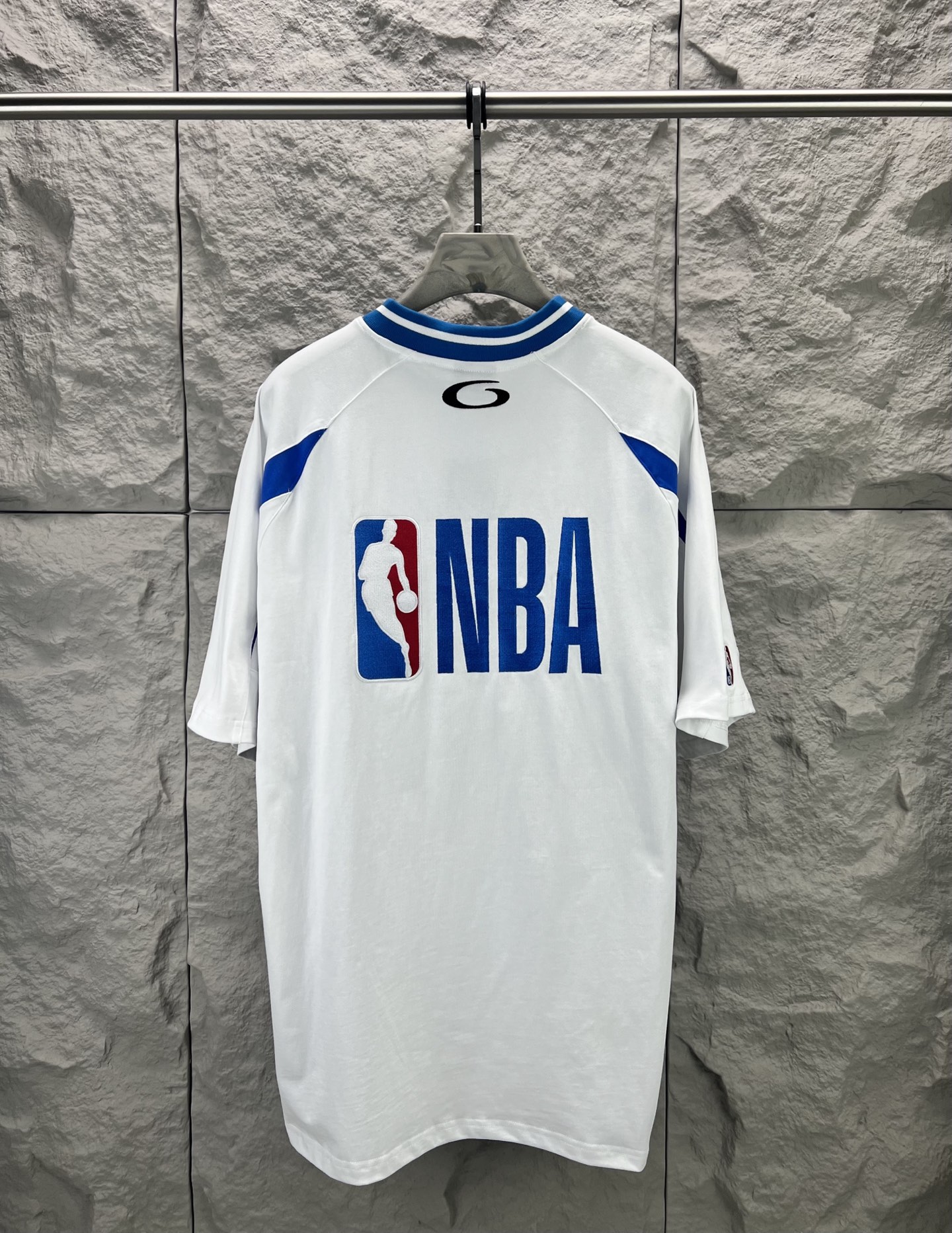Balenciaga BALENCI*GA × NBA SS26联名T恤 采用科技网眼面料 经透气排汗工艺处理 兼具运动功能性与 廓形 衣身主体为黑色 肩部与袖口拼接撞色饰带 采用精密车缝工艺 线条利落 正面“BALENCIAGA”字样与数字“10”采用立体植绒或贴布绣工艺 边缘锁边牢固 不易脱线 领口为罗纹圆领 采用高弹氨纶混纺材质 久穿不易变形 下摆与袖口采用双针锁边工艺 提升整体耐用性 衣身印有NBA 标识 采用环保胶印工艺 图案清晰牢固 整体设计融合高端时装与运动元素 兼顾舒适穿着与视觉张力 适合潮流穿搭与收藏 整体走线平直细腻 面料舒适柔软 颜色一致无色差 能与同款搭配营造 造型 驾驭各种场合 定制辅料 三标齐全