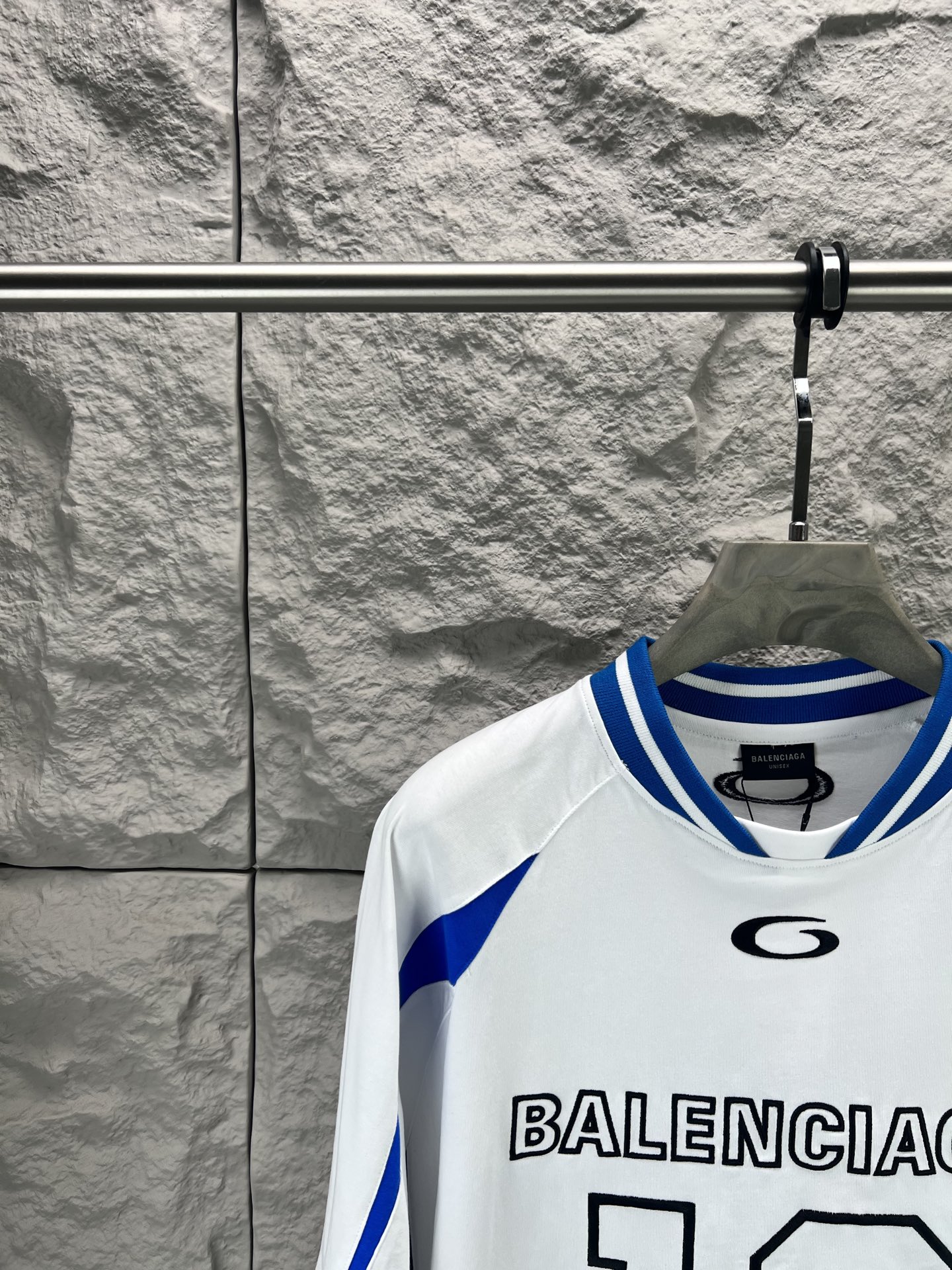 Balenciaga BALENCI*GA × NBA SS26联名T恤 采用科技网眼面料 经透气排汗工艺处理 兼具运动功能性与 廓形 衣身主体为黑色 肩部与袖口拼接撞色饰带 采用精密车缝工艺 线条利落 正面“BALENCIAGA”字样与数字“10”采用立体植绒或贴布绣工艺 边缘锁边牢固 不易脱线 领口为罗纹圆领 采用高弹氨纶混纺材质 久穿不易变形 下摆与袖口采用双针锁边工艺 提升整体耐用性 衣身印有NBA 标识 采用环保胶印工艺 图案清晰牢固 整体设计融合高端时装与运动元素 兼顾舒适穿着与视觉张力 适合潮流穿搭与收藏 整体走线平直细腻 面料舒适柔软 颜色一致无色差 能与同款搭配营造 造型 驾驭各种场合 定制辅料 三标齐全