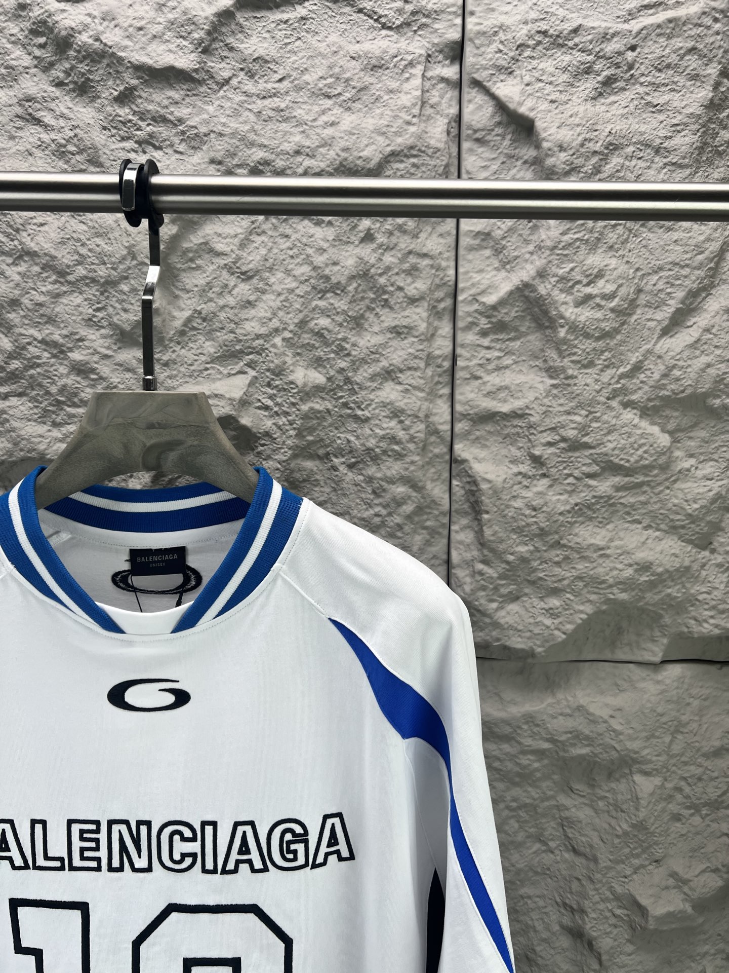 Balenciaga BALENCI*GA × NBA SS26联名T恤 采用科技网眼面料 经透气排汗工艺处理 兼具运动功能性与 廓形 衣身主体为黑色 肩部与袖口拼接撞色饰带 采用精密车缝工艺 线条利落 正面“BALENCIAGA”字样与数字“10”采用立体植绒或贴布绣工艺 边缘锁边牢固 不易脱线 领口为罗纹圆领 采用高弹氨纶混纺材质 久穿不易变形 下摆与袖口采用双针锁边工艺 提升整体耐用性 衣身印有NBA 标识 采用环保胶印工艺 图案清晰牢固 整体设计融合高端时装与运动元素 兼顾舒适穿着与视觉张力 适合潮流穿搭与收藏 整体走线平直细腻 面料舒适柔软 颜色一致无色差 能与同款搭配营造 造型 驾驭各种场合 定制辅料 三标齐全