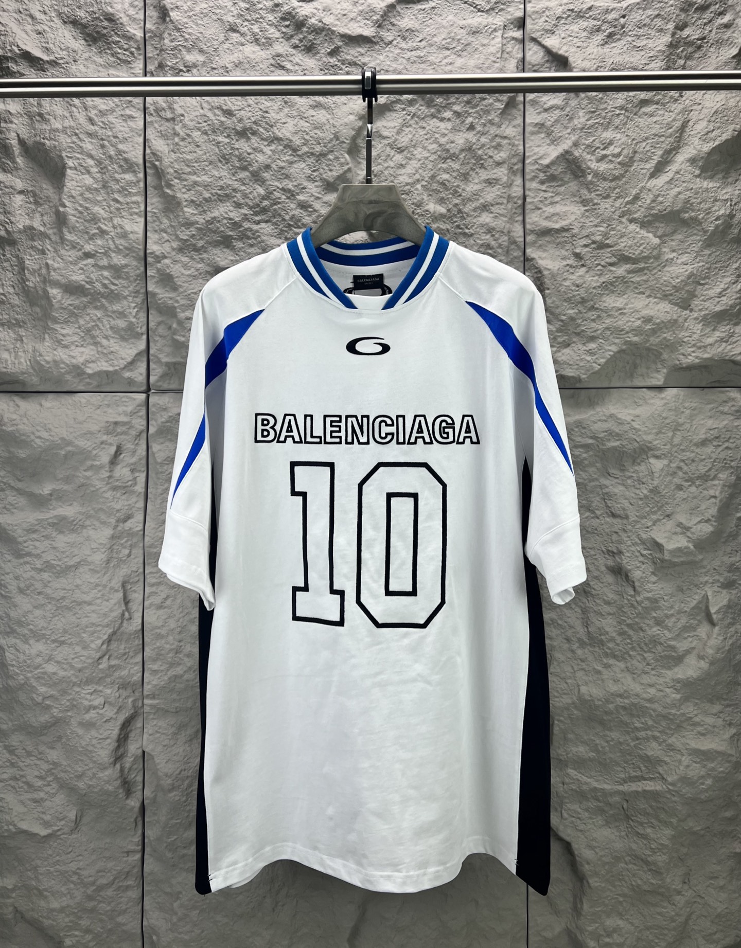 Balenciaga BALENCI*GA × NBA SS26联名T恤 采用科技网眼面料 经透气排汗工艺处理 兼具运动功能性与 廓形 衣身主体为黑色 肩部与袖口拼接撞色饰带 采用精密车缝工艺 线条利落 正面“BALENCIAGA”字样与数字“10”采用立体植绒或贴布绣工艺 边缘锁边牢固 不易脱线 领口为罗纹圆领 采用高弹氨纶混纺材质 久穿不易变形 下摆与袖口采用双针锁边工艺 提升整体耐用性 衣身印有NBA 标识 采用环保胶印工艺 图案清晰牢固 整体设计融合高端时装与运动元素 兼顾舒适穿着与视觉张力 适合潮流穿搭与收藏 整体走线平直细腻 面料舒适柔软 颜色一致无色差 能与同款搭配营造 造型 驾驭各种场合 定制辅料 三标齐全