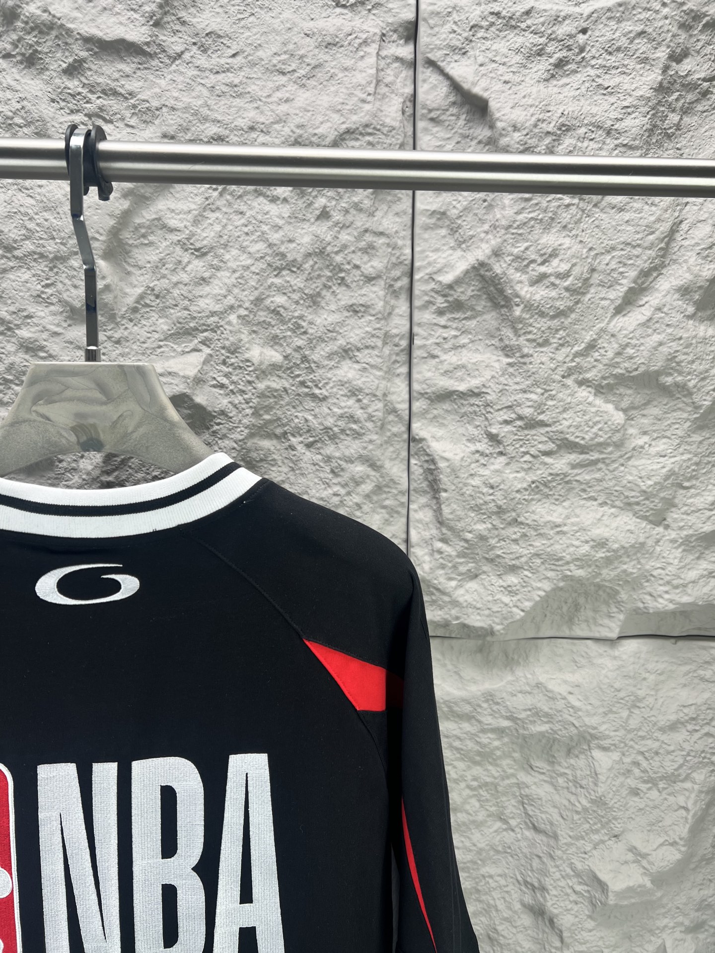 Balenciaga BALENCI*GA × NBA SS26联名T恤 采用科技网眼面料 经透气排汗工艺处理 兼具运动功能性与 廓形 衣身主体为黑色 肩部与袖口拼接撞色饰带 采用精密车缝工艺 线条利落 正面“BALENCIAGA”字样与数字“10”采用立体植绒或贴布绣工艺 边缘锁边牢固 不易脱线 领口为罗纹圆领 采用高弹氨纶混纺材质 久穿不易变形 下摆与袖口采用双针锁边工艺 提升整体耐用性 衣身印有NBA 标识 采用环保胶印工艺 图案清晰牢固 整体设计融合高端时装与运动元素 兼顾舒适穿着与视觉张力 适合潮流穿搭与收藏 整体走线平直细腻 面料舒适柔软 颜色一致无色差 能与同款搭配营造 造型 驾驭各种场合 定制辅料 三标齐全